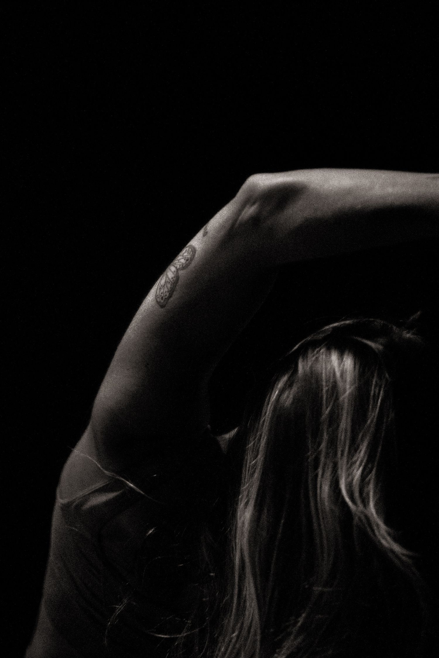 Dramatic black and white portrait of a dancer stretching in moody lighting against dark background.