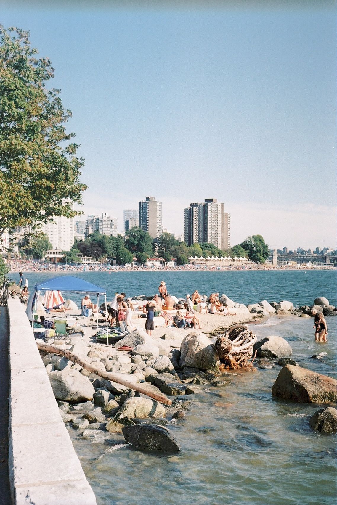 Urban beach with people lounging on rocks by the water with high-rise buildings in the background.