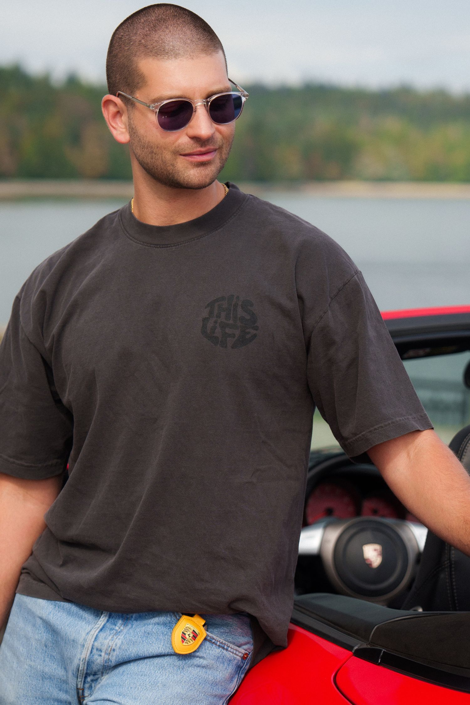 Person in dark t-shirt and sunglasses leaning against red sports car.