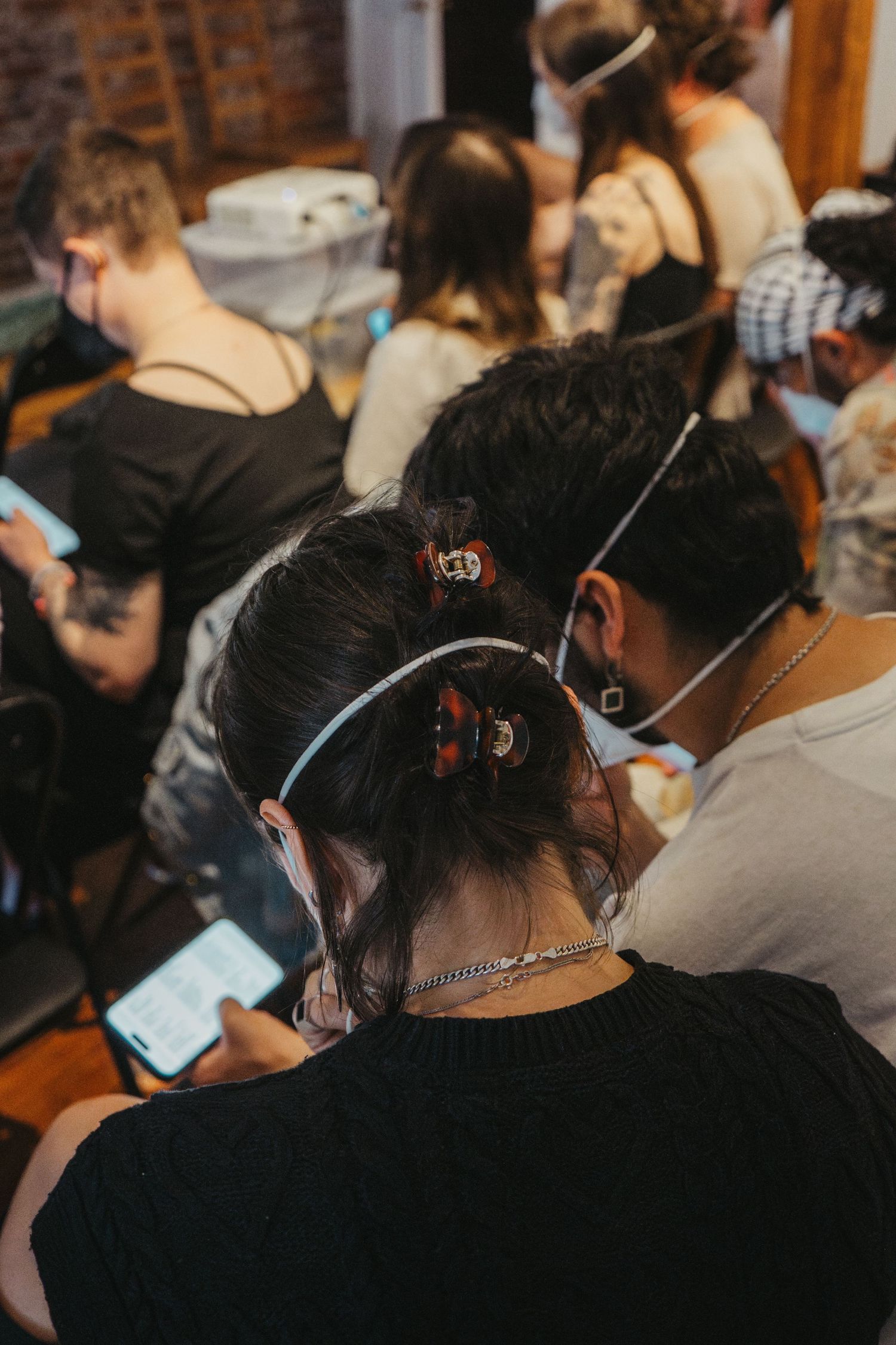 Group of people wearing masks look at their phones while sitting together indoors.