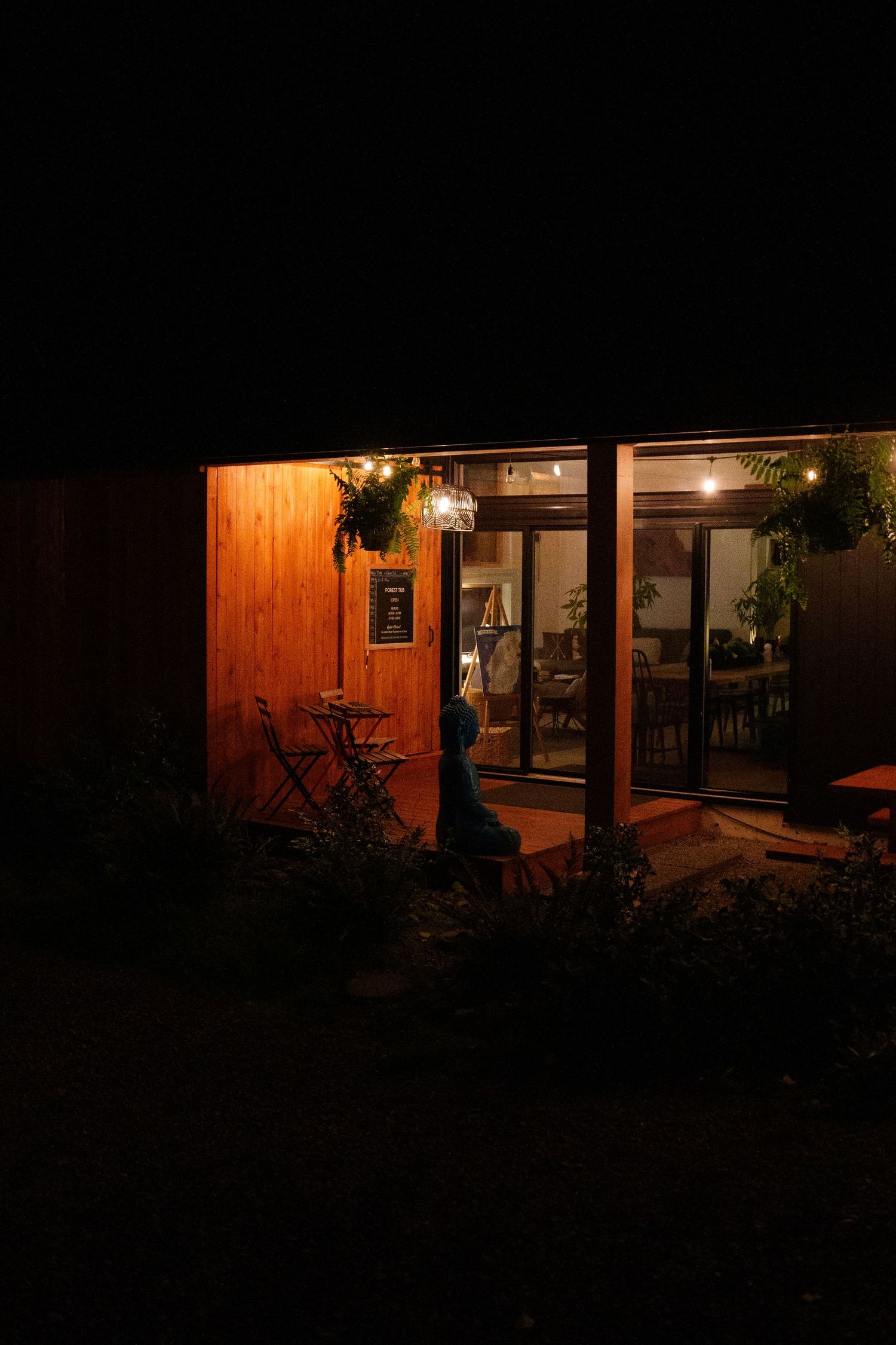 Warmly lit wooden cabin exterior with glass doors and hanging lantern at night.