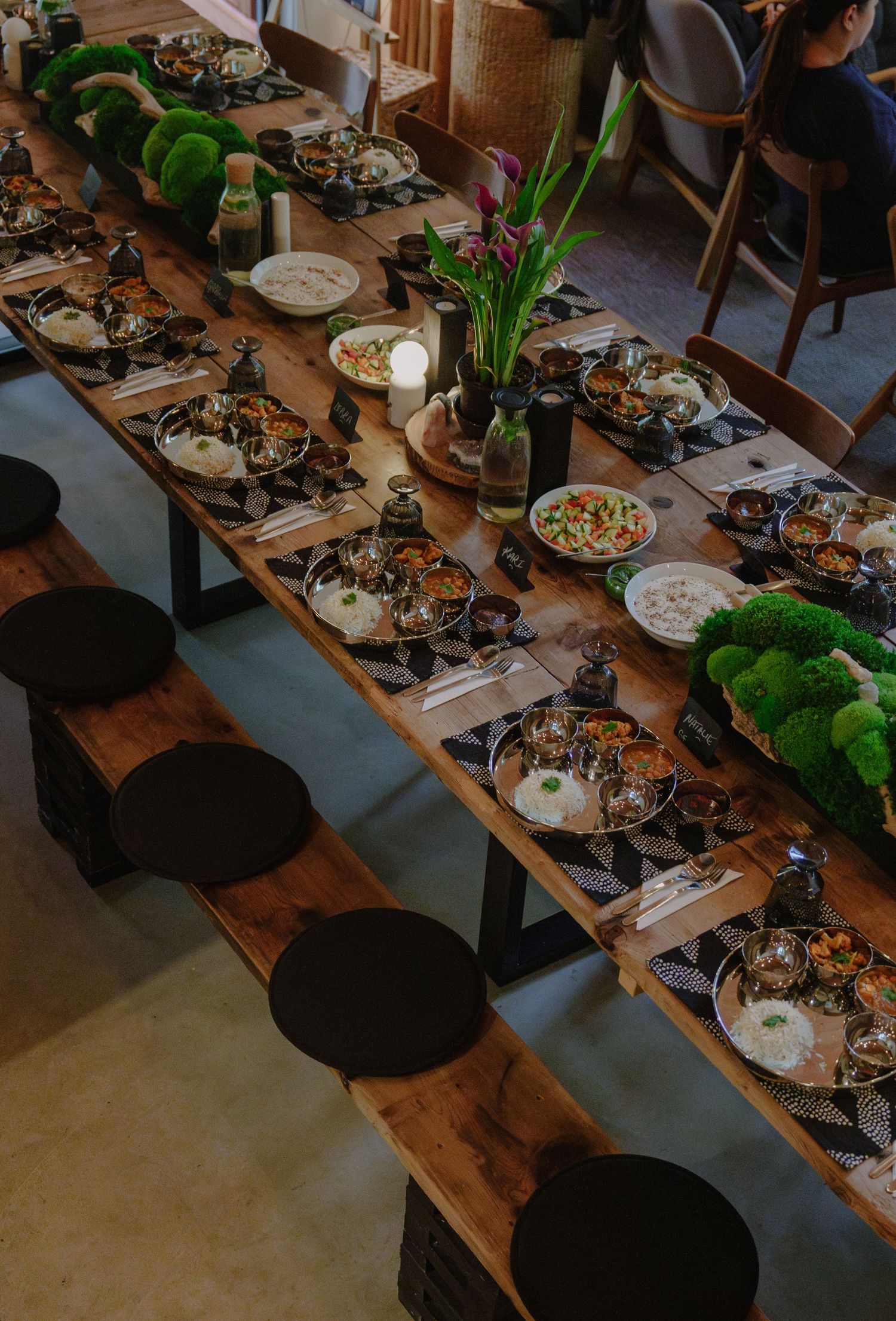 A long wooden table set with plates, moss decorations and potted plants for an elegant dinner gathering.