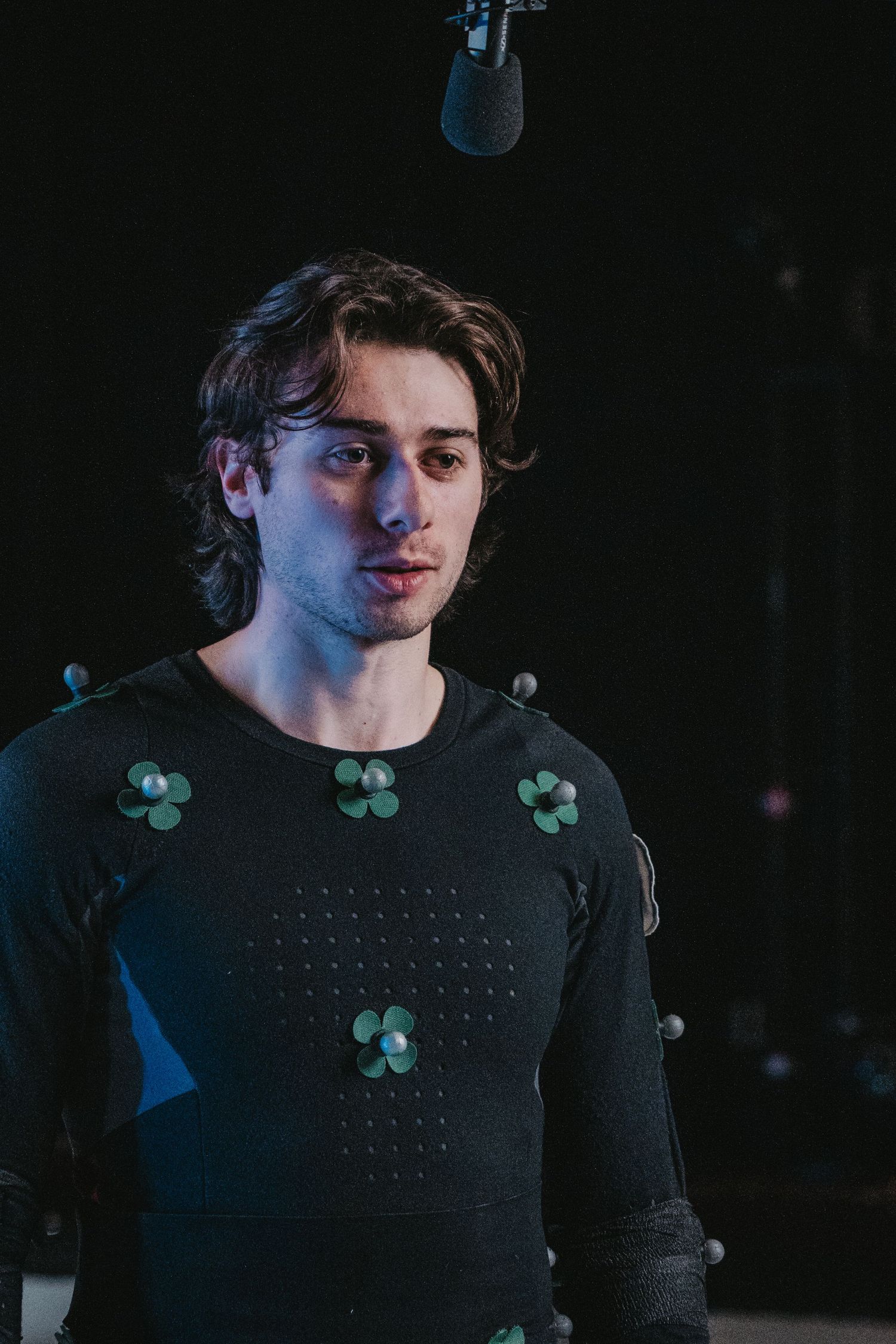 Close-up shot of motion capture suit with green tracking markers in dimly lit studio.