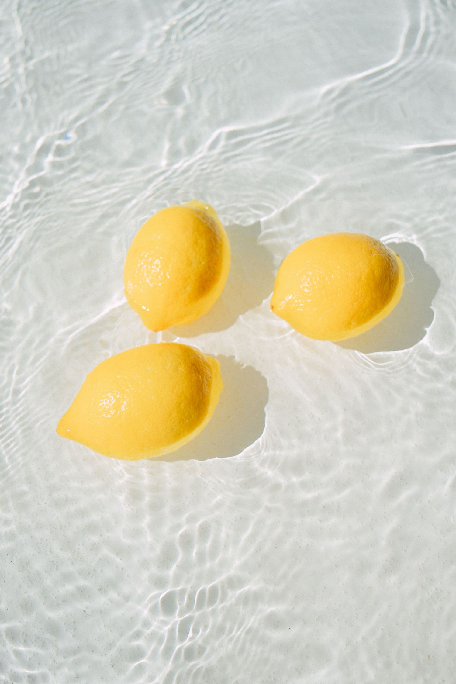 Three bright yellow lemons floating in rippling clear water.