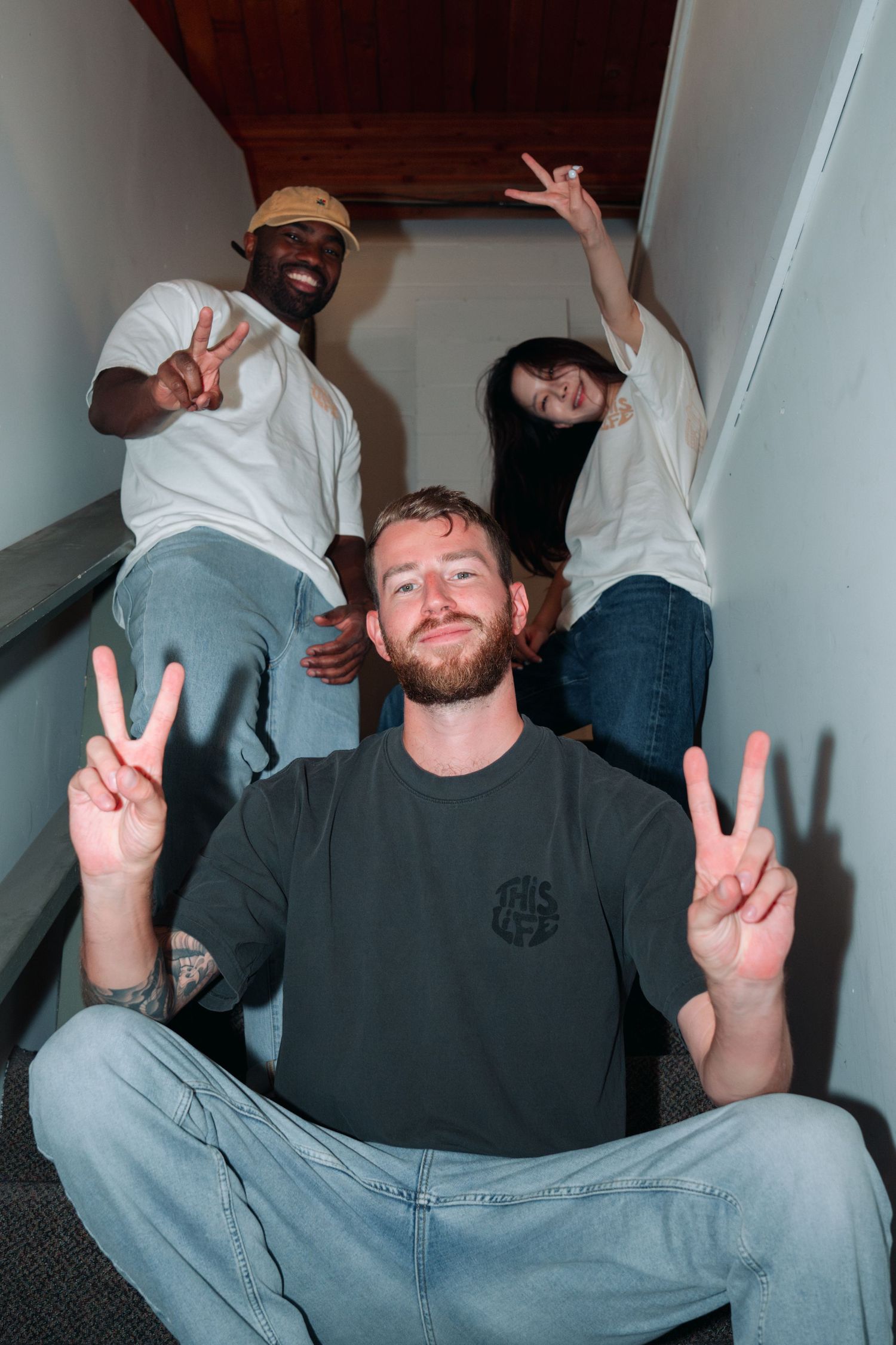 Three friends posing together on a staircase making peace signs and smiling at the camera.