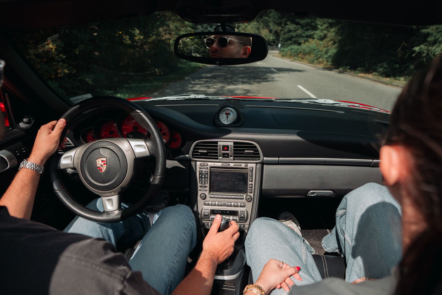 Interior view of a Porsche dashboard while driving through trees.