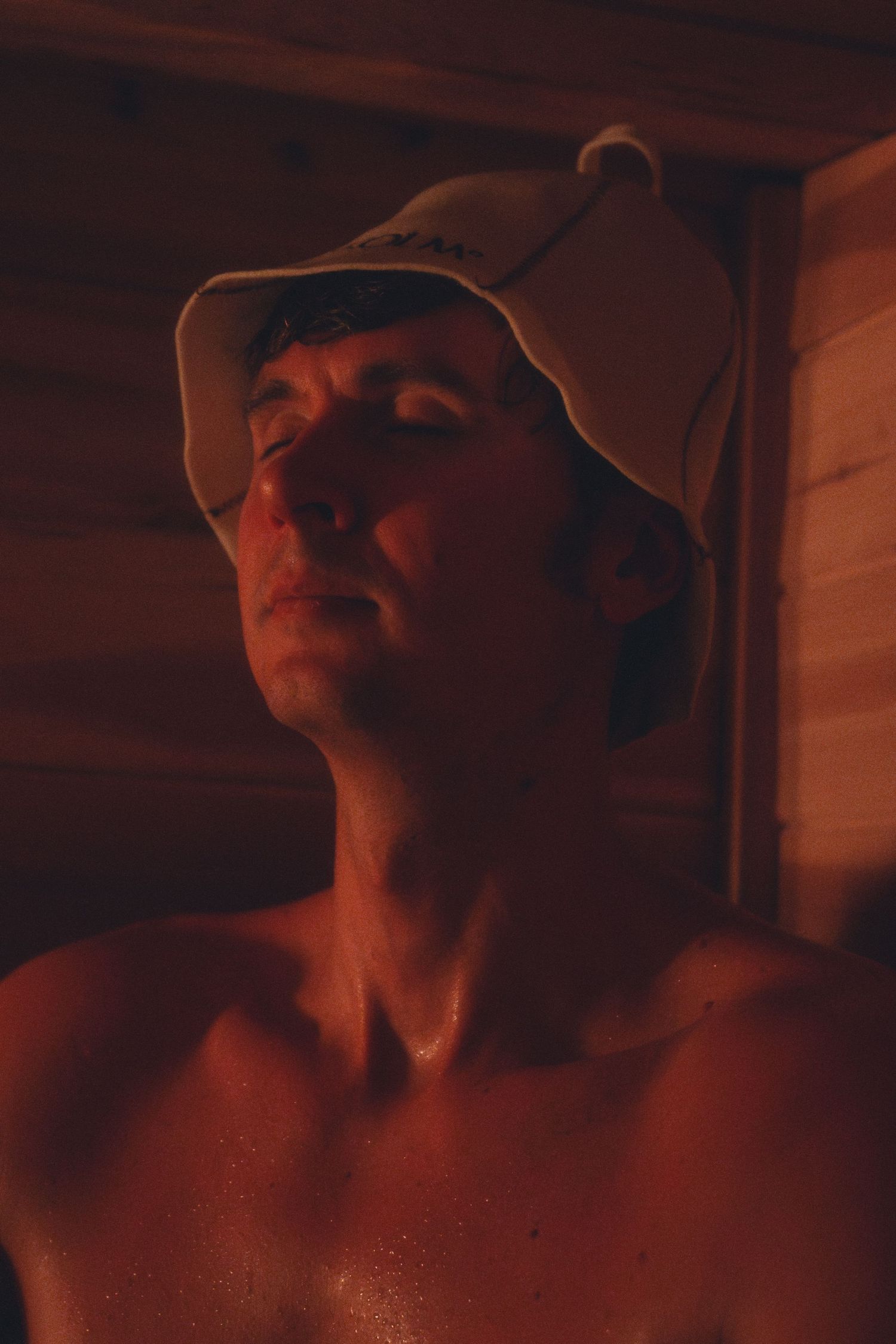 Dramatic side profile portrait in bucket hat with warm red lighting.