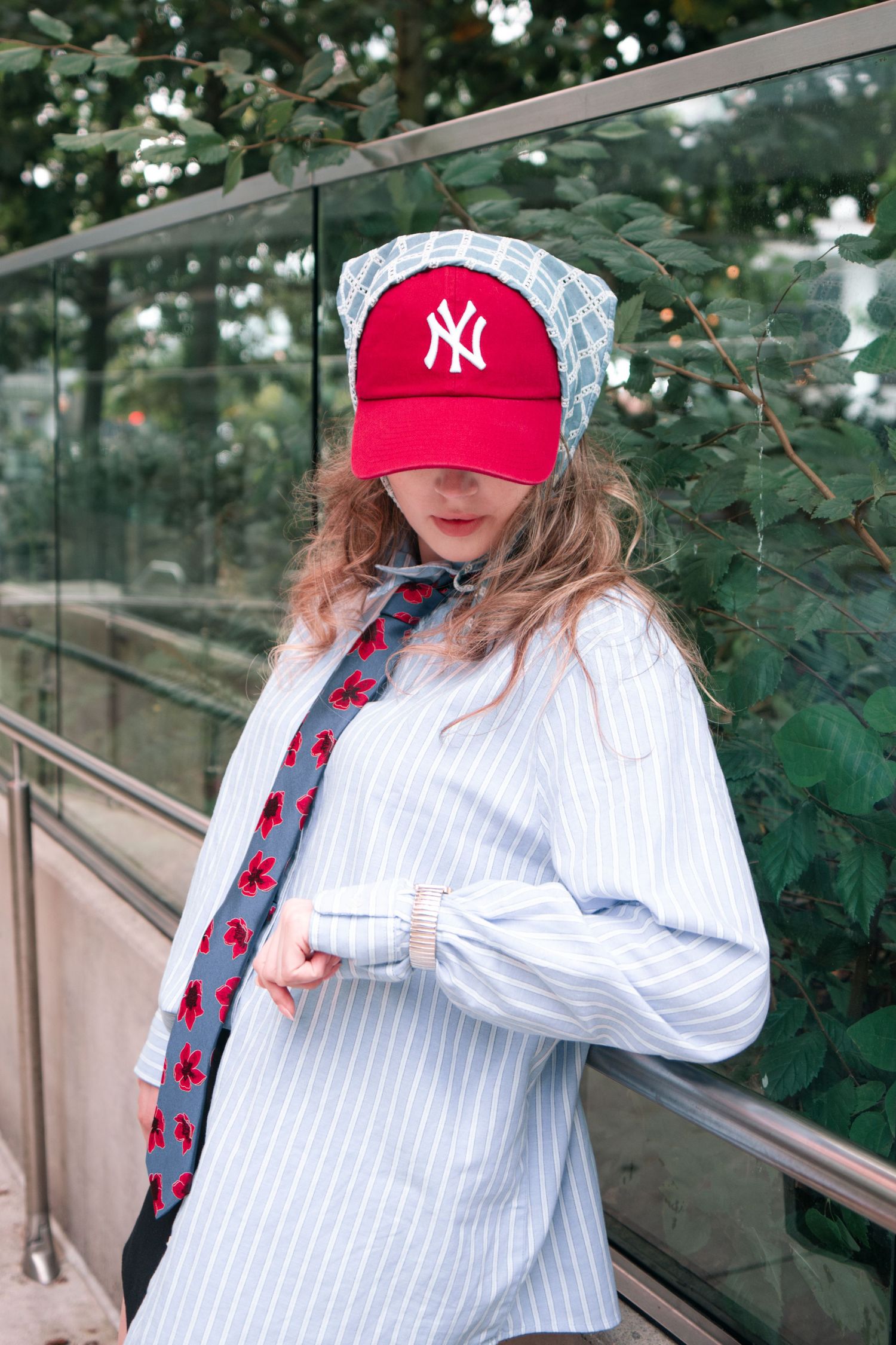 Stylish outfit with red Yankees cap, striped shirt and floral tie against green foliage.