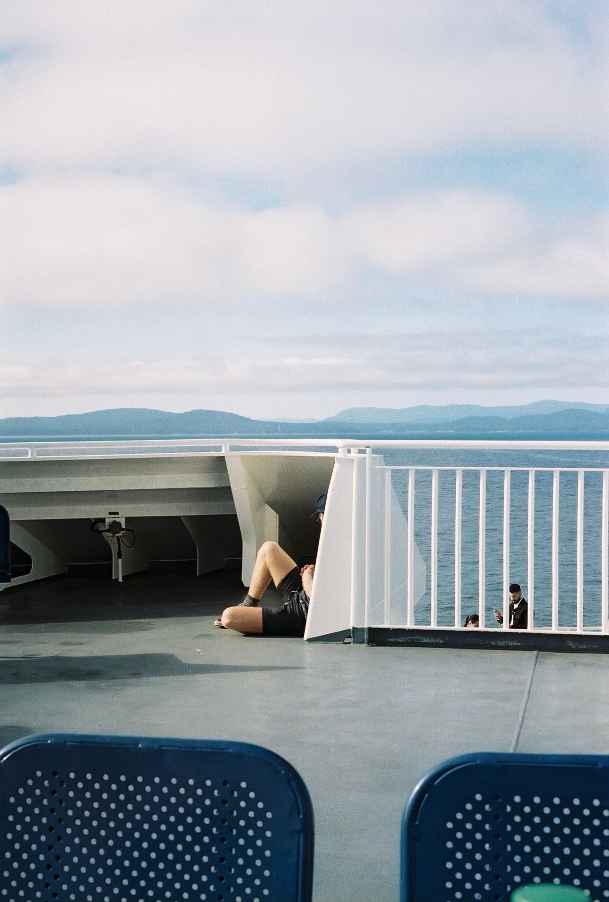 Person relaxing on ferry deck with distant mountains visible across calm waters.
