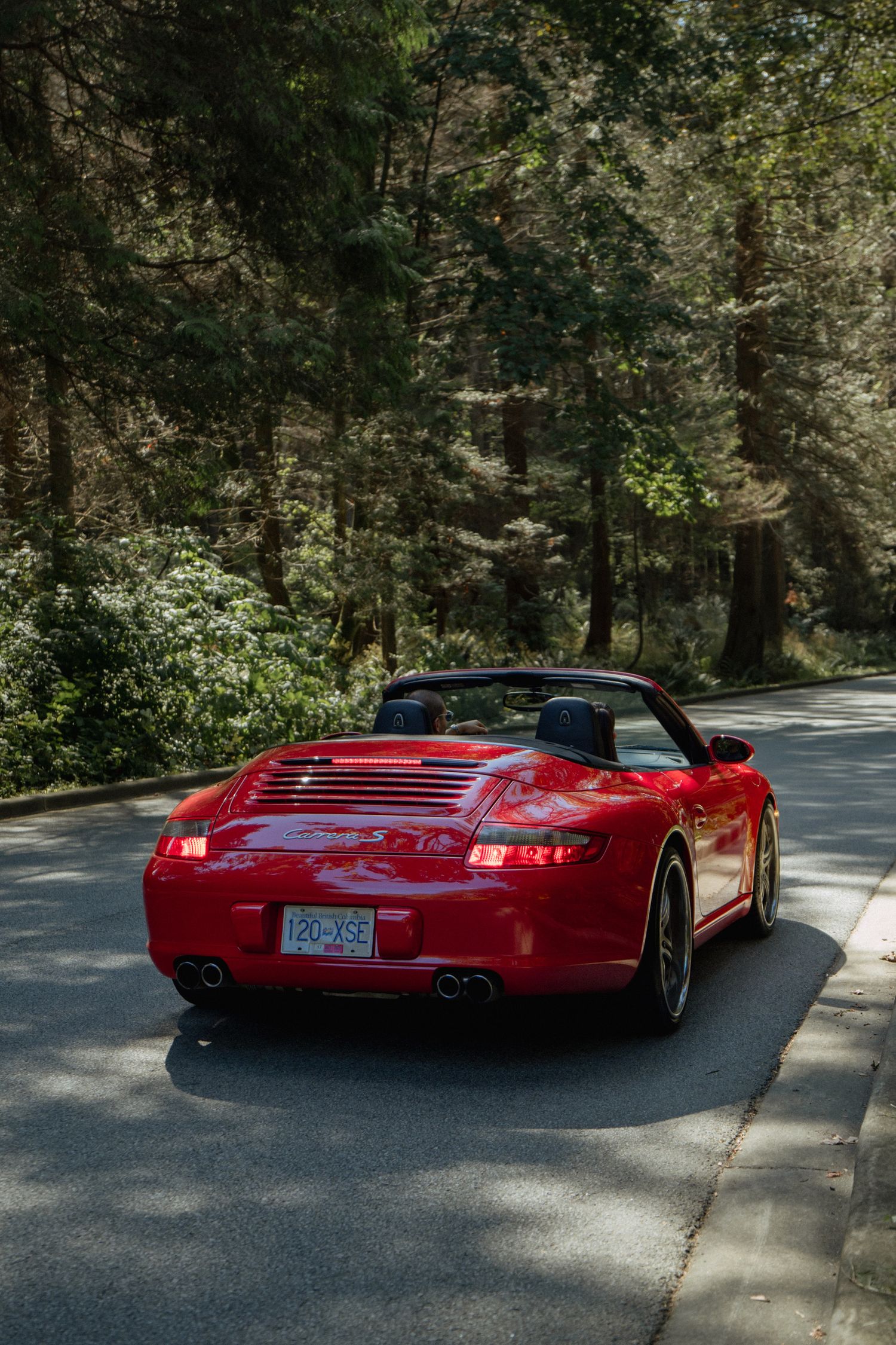 Red Porsche 911 driving through a winding forest road.