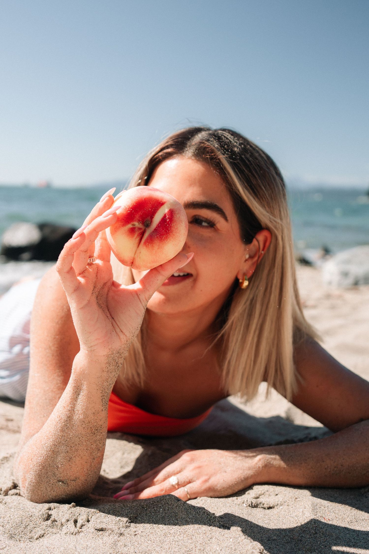 Person holding peach while relaxing on sandy beach with ocean view.