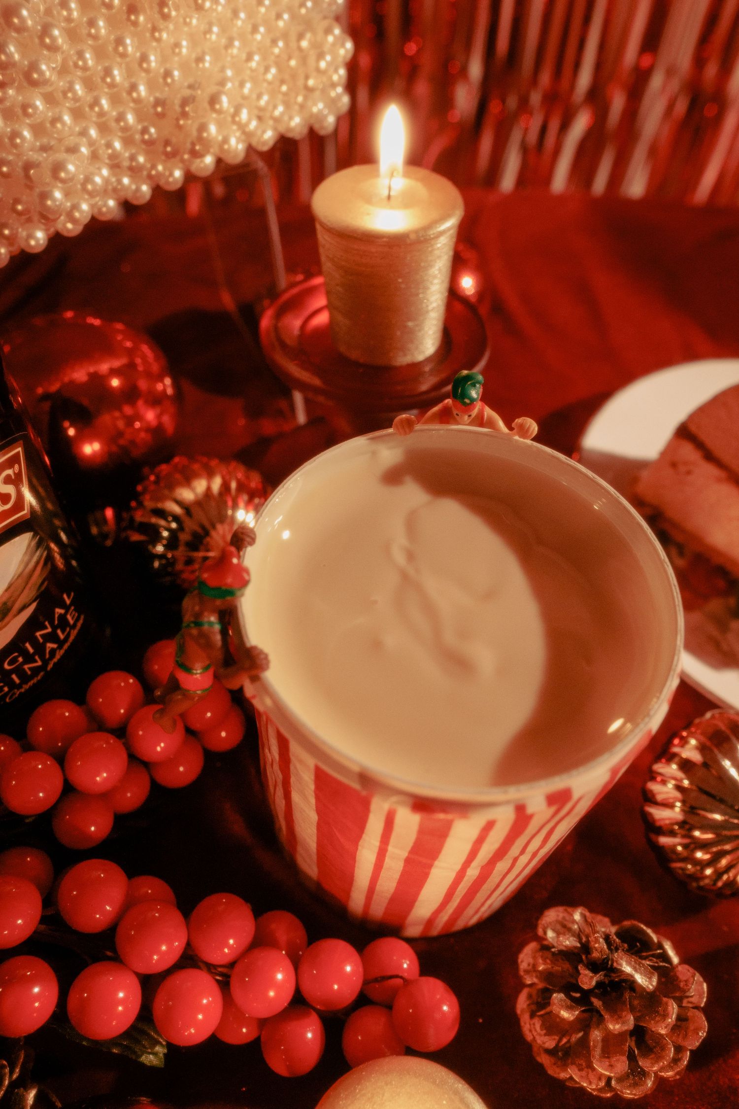 Holiday table setting with lit candle, pinecone, and red berries against warm lighting.