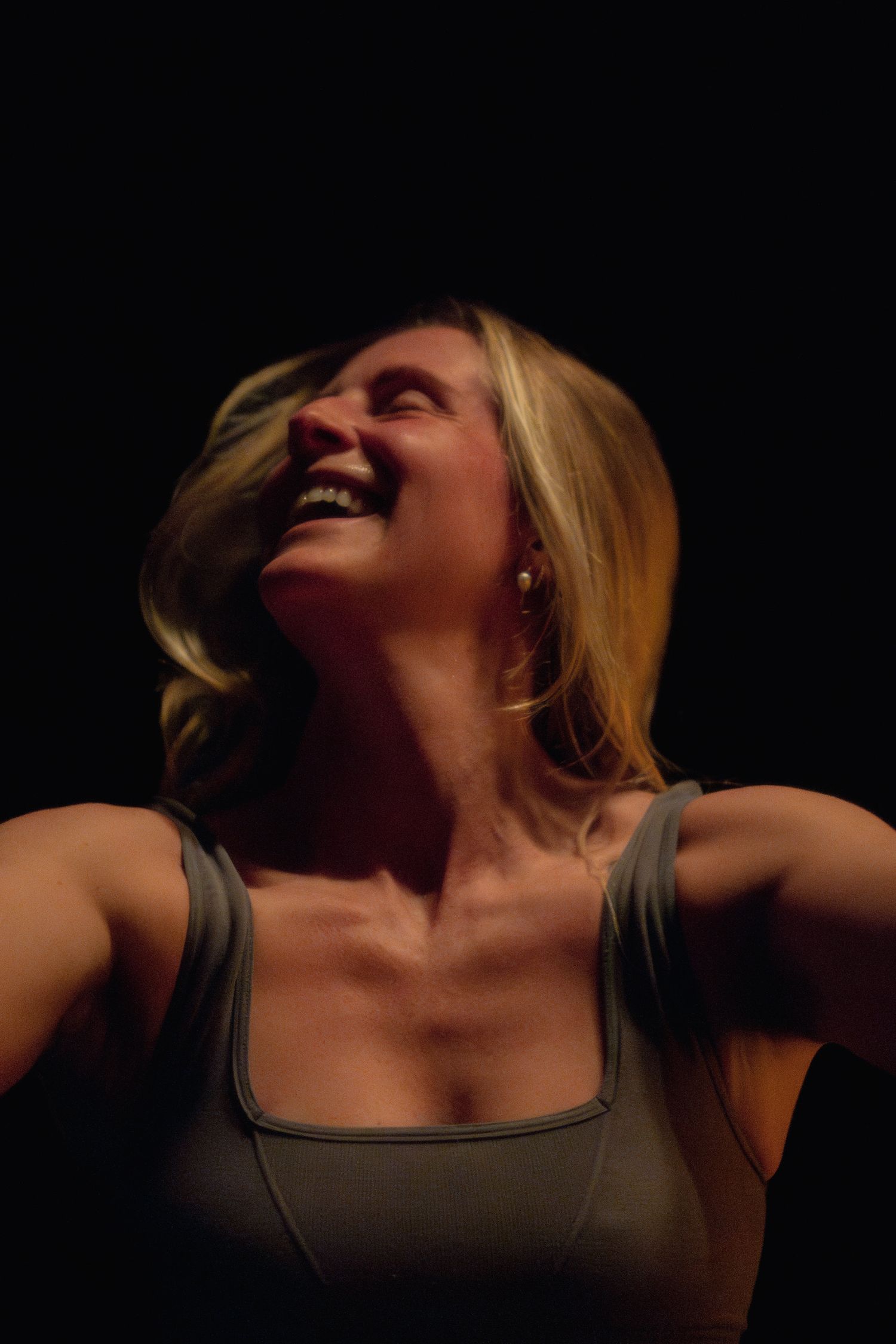 Joyful dancer in gray tank top photographed against dark background with dramatic lighting.