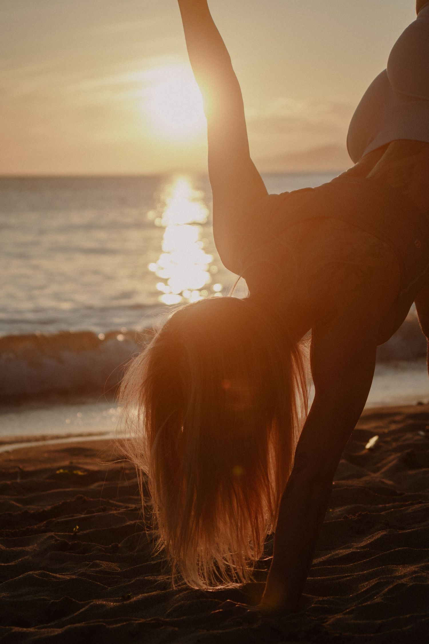 Athletic figure bends backwards in graceful pose against golden sunset over ocean.