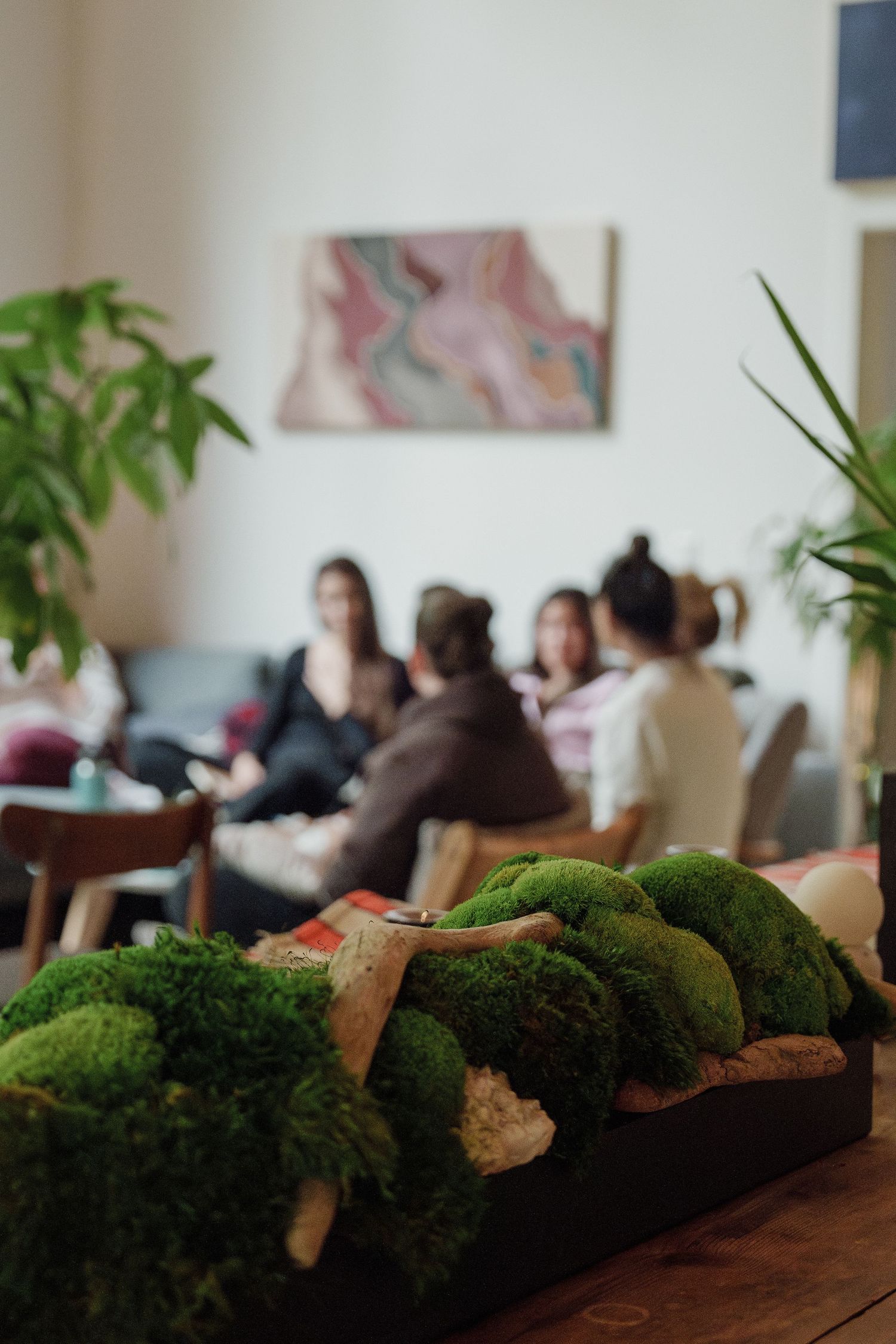 Indoor plants and broccoli arrangements with a blurred group gathering in the background.