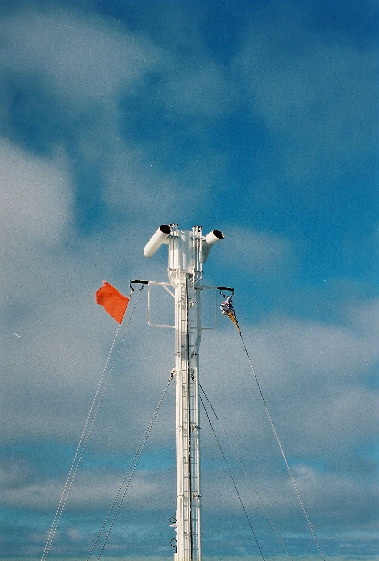 Weather monitoring equipment and red flag on white pole against blue sky.