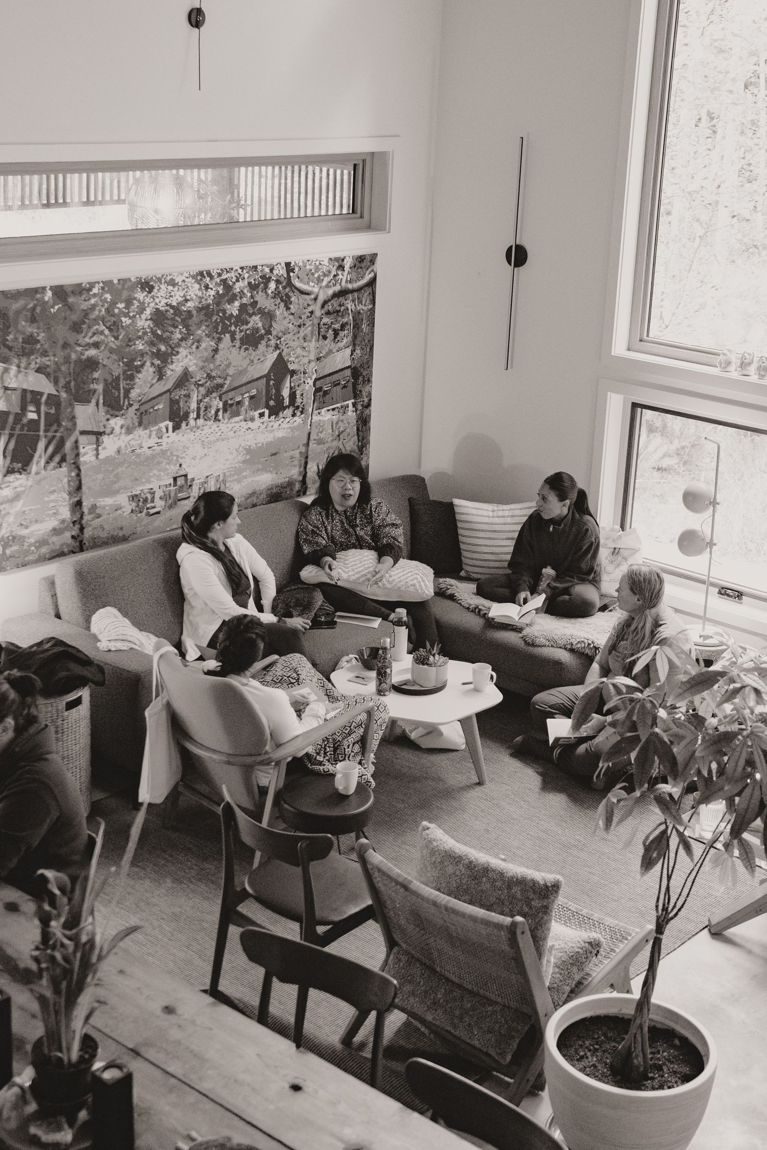 Black and white photo of casual indoor gathering with vintage furniture and plants.