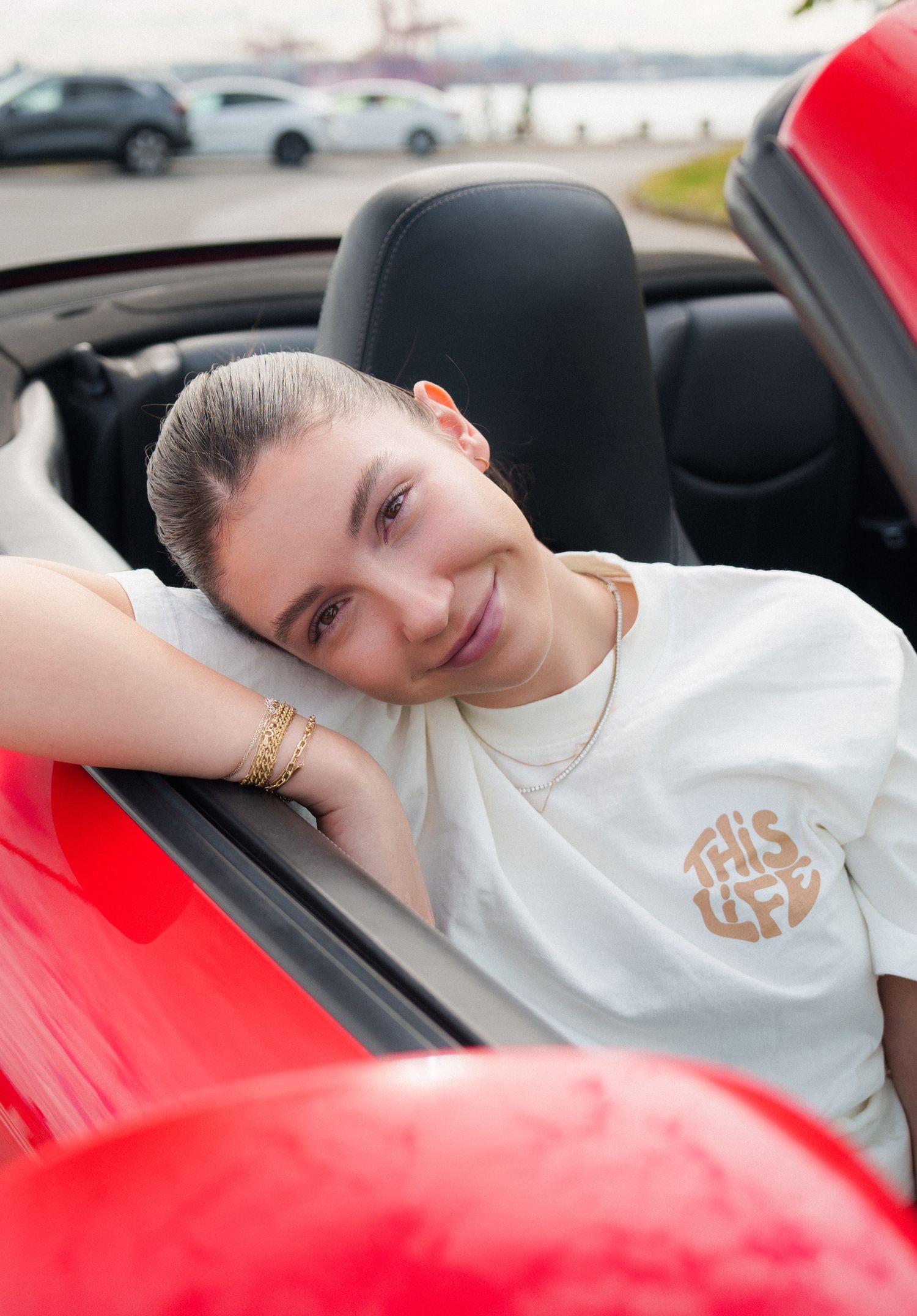 Person in white t-shirt relaxing in red convertible sports car.