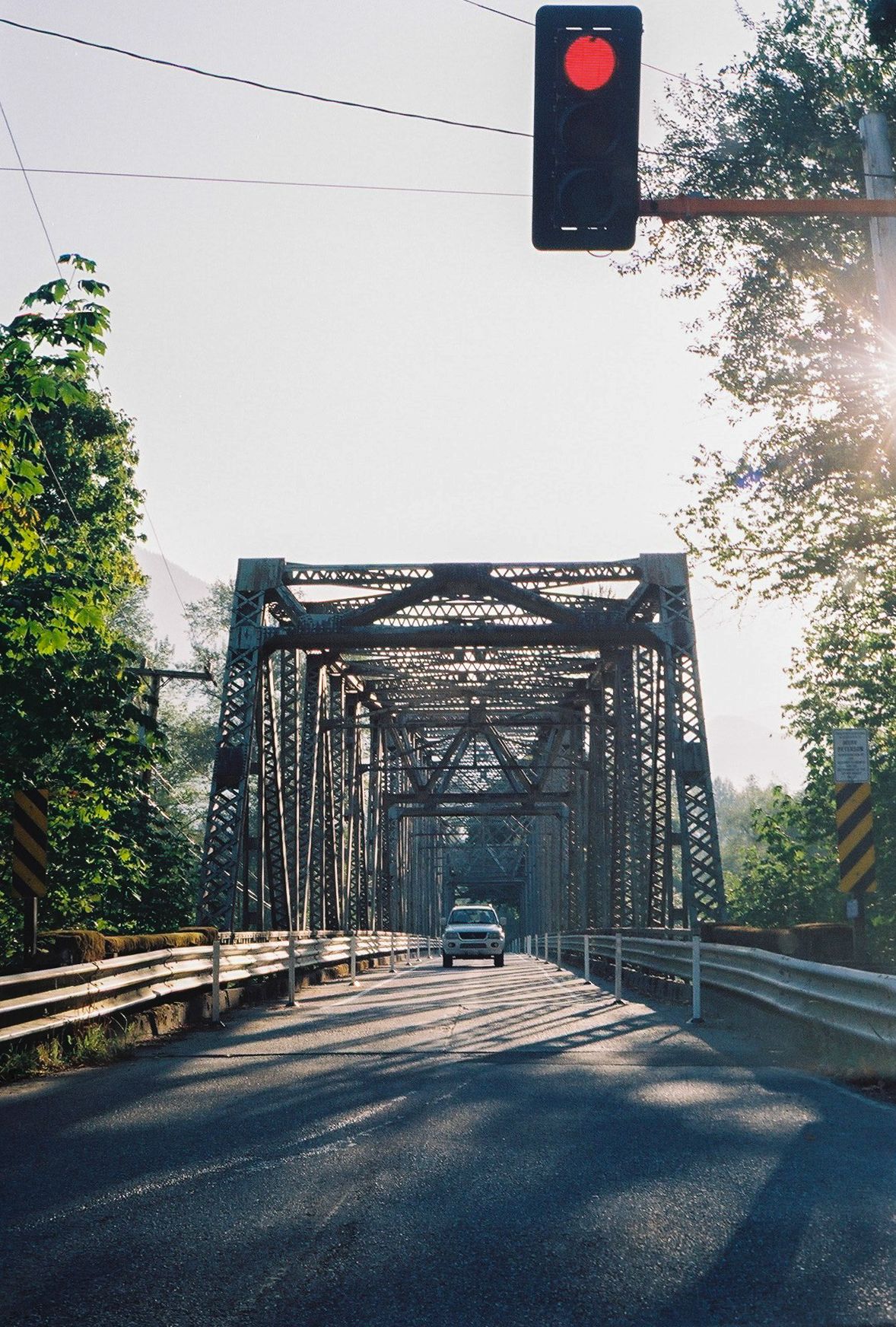 Steel truss bridge with car crossing under red traffic light.