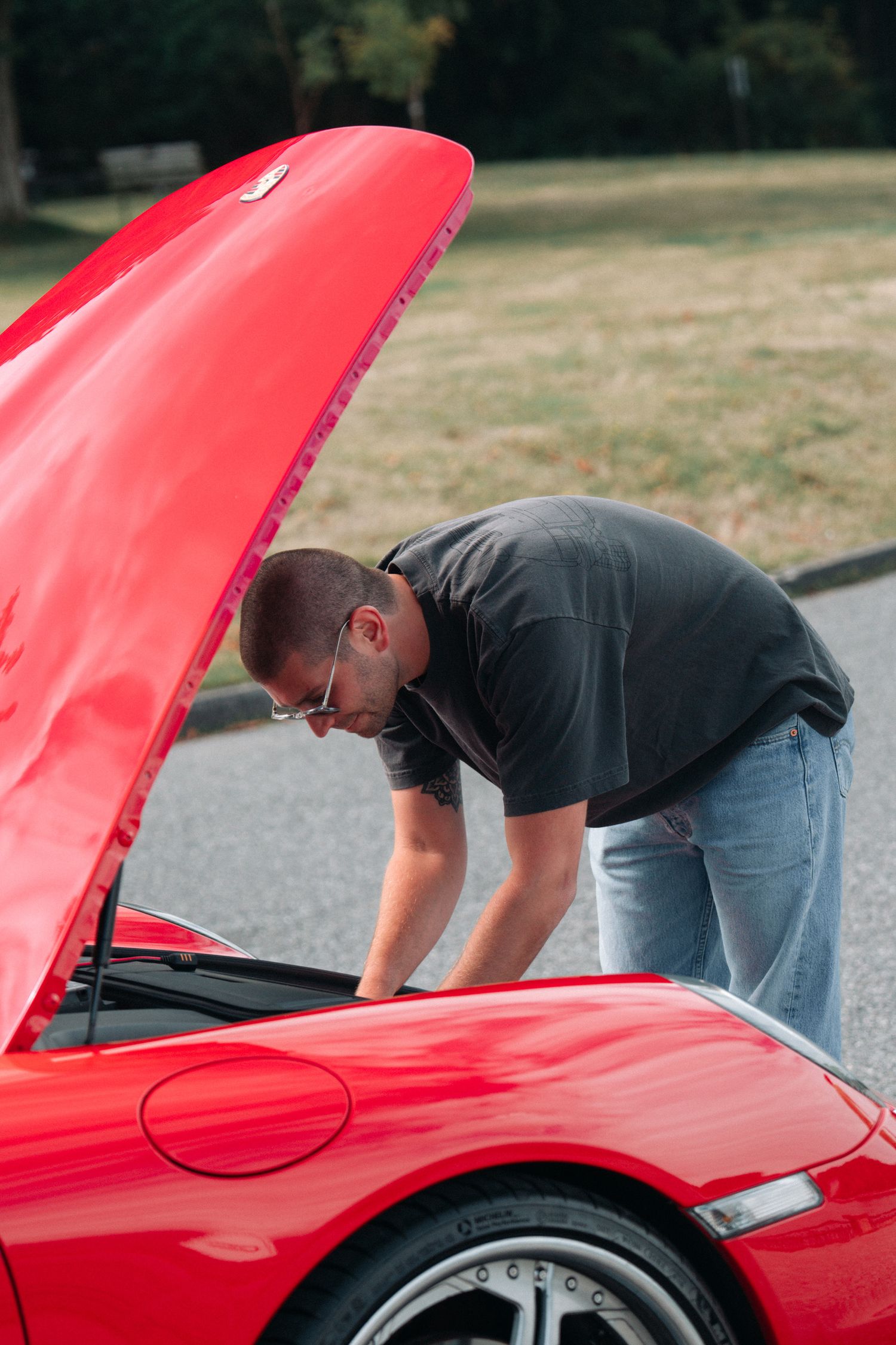 Person checking under the hood of a red Porsche sports car.
