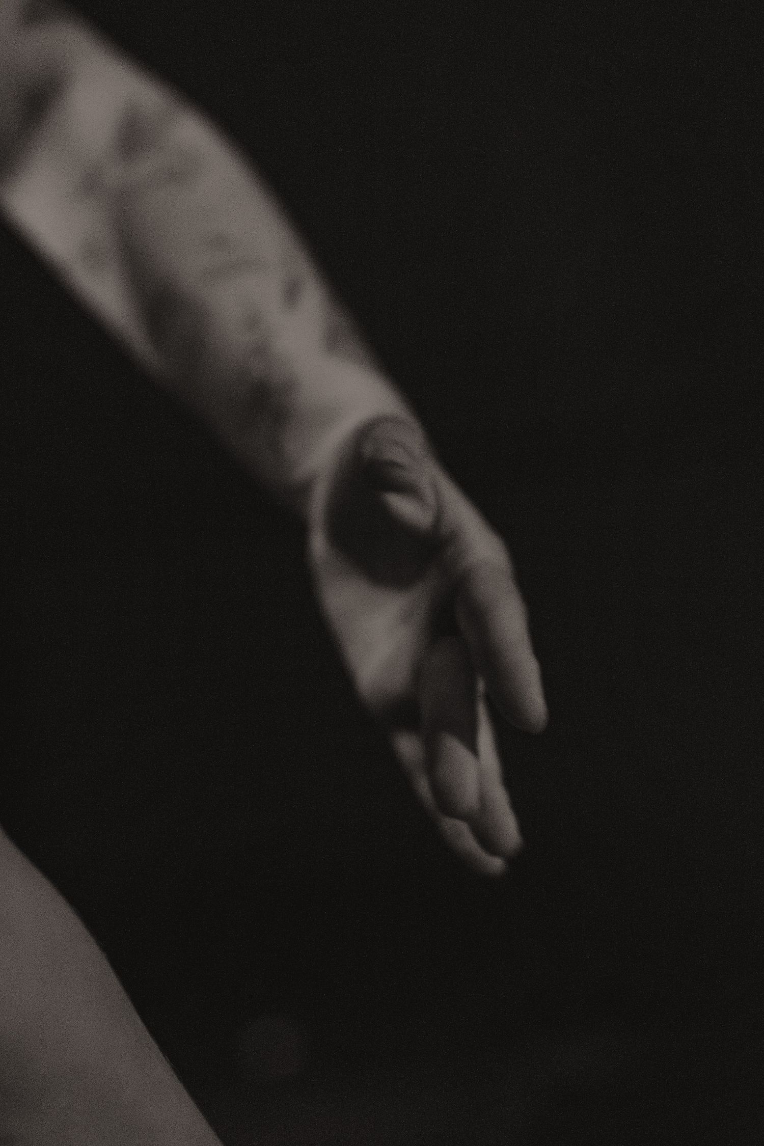 Moody black and white photo of an outstretched hand with tattoos against dark background.