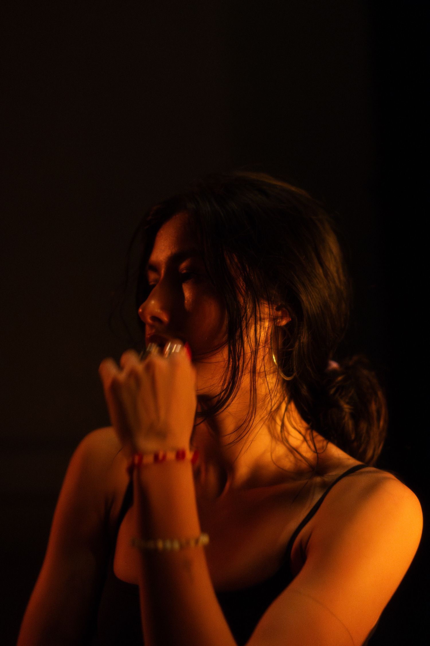 Candid portrait in warm low light showing contemplative pose with bracelets.