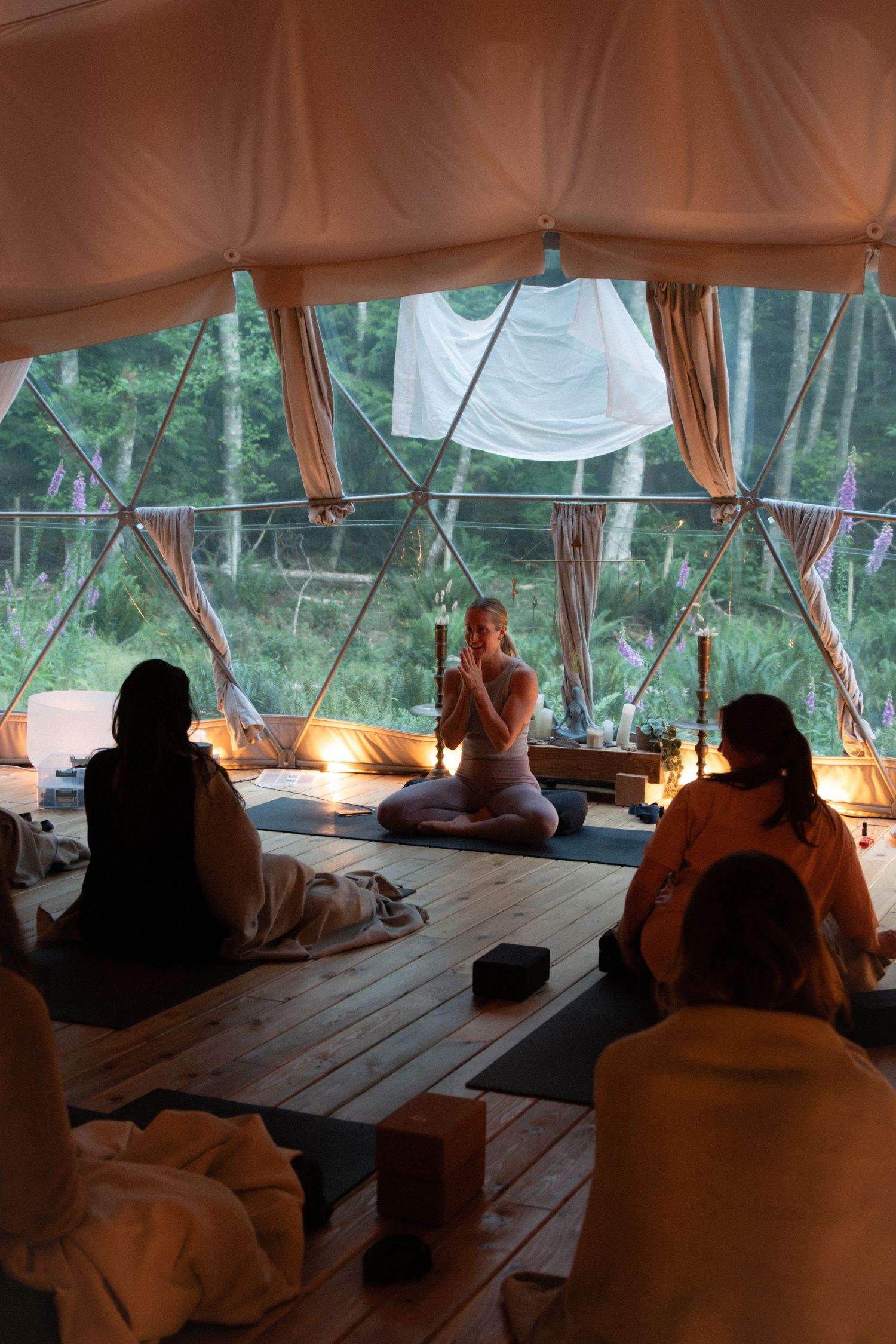 Peaceful yoga or meditation gathering in a light-filled dome tent surrounded by forest.