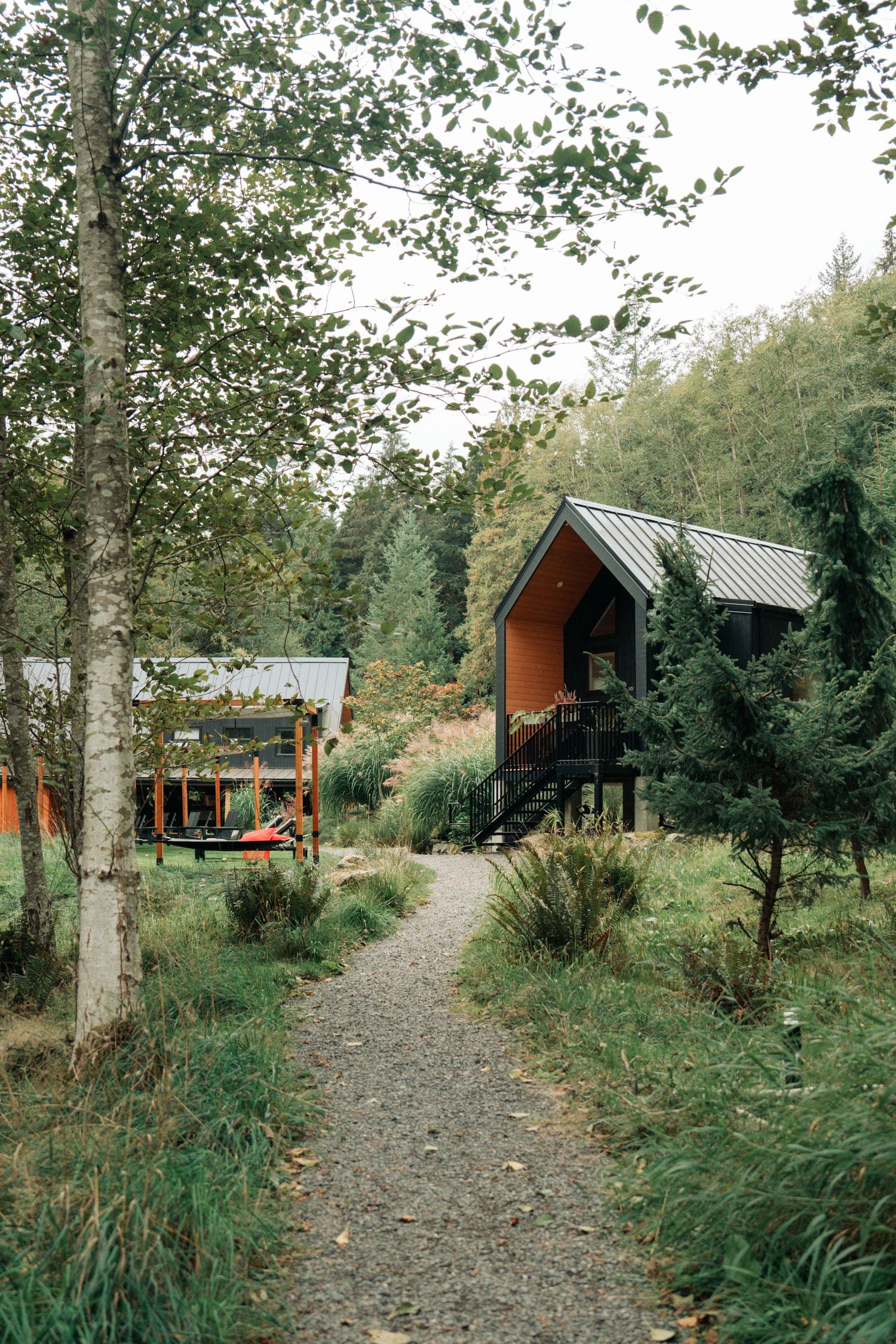 Woodland path leading to an orange A-frame cabin with green surroundings.