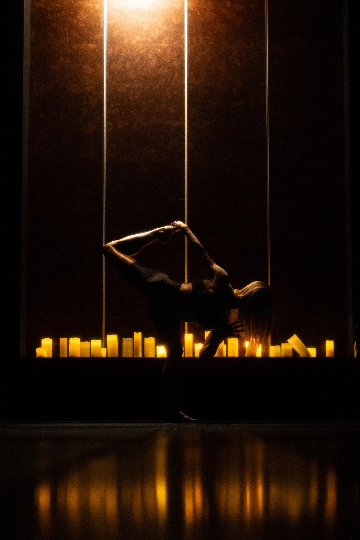 Artistic dance performance with candles creating dramatic silhouette and reflection.