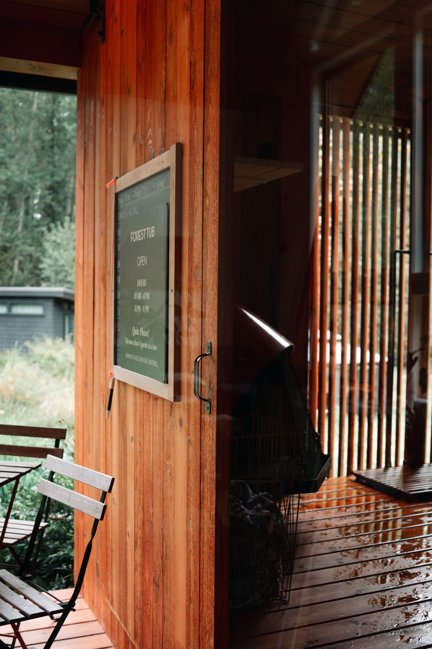 Wooden porch entrance with chalkboard sign and folding chair in natural outdoor setting.