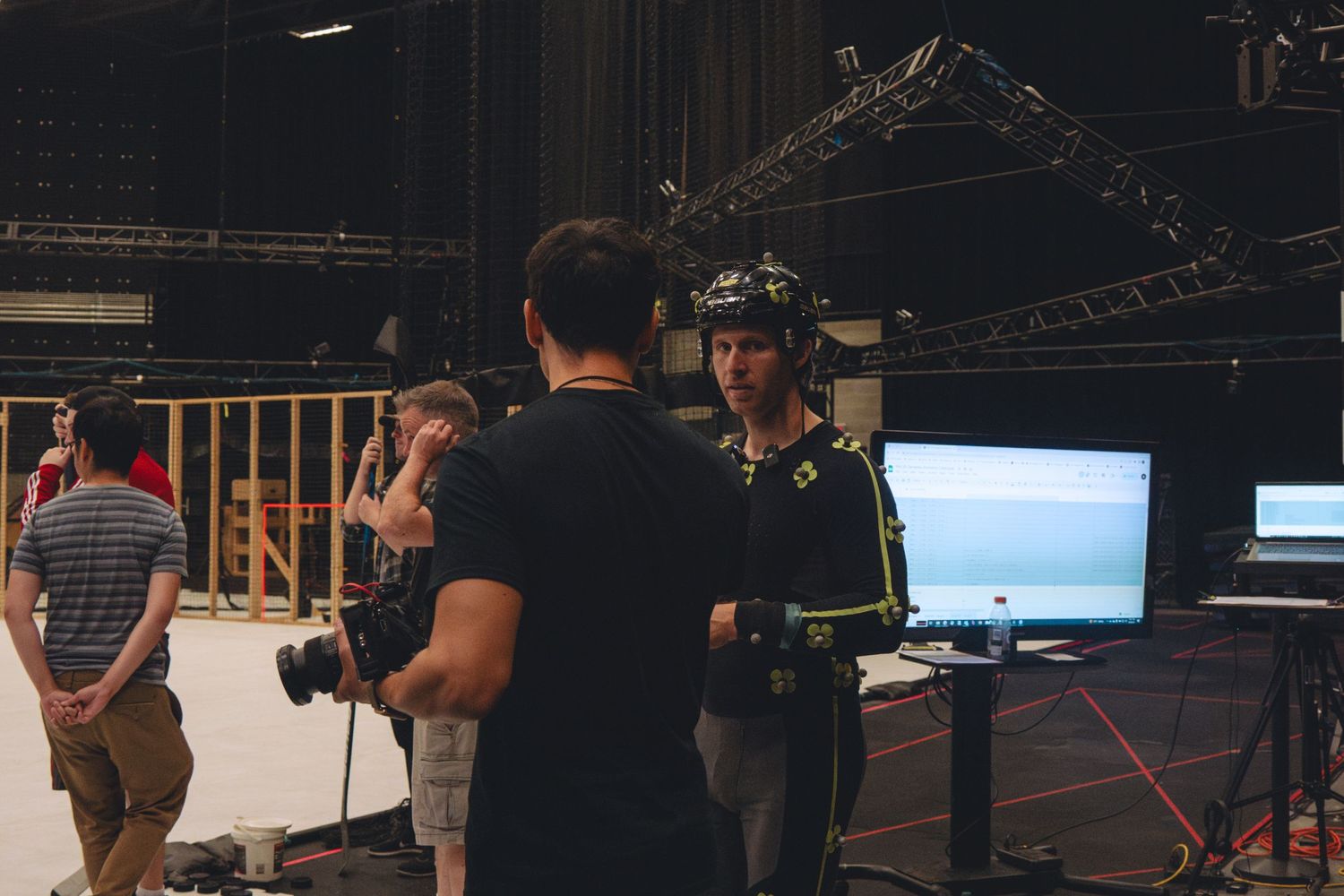Behind-the-scenes crew members work with motion capture equipment in a dark studio setting.