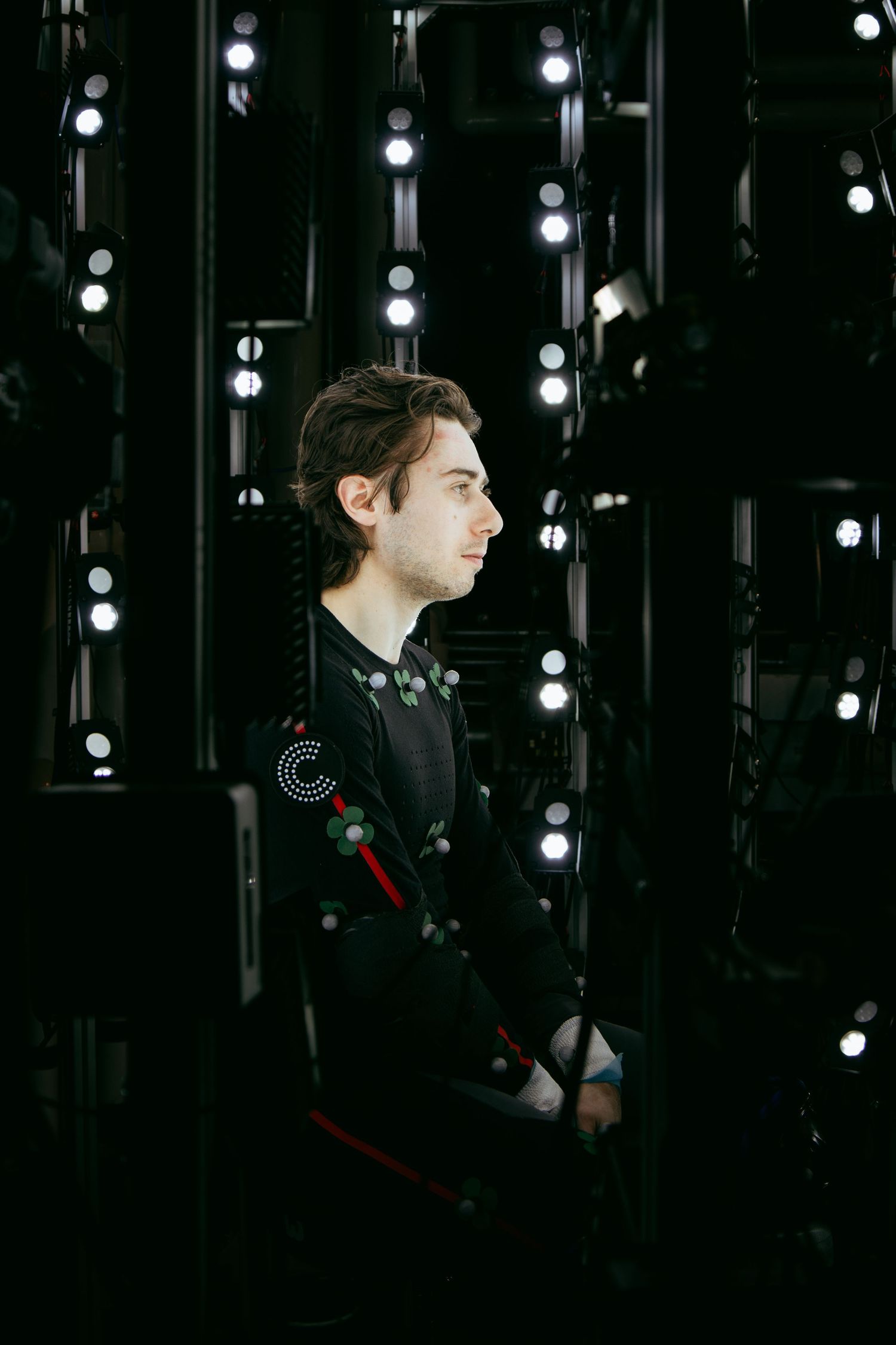 Side profile shot of performer in motion capture suit against backdrop of studio lights.