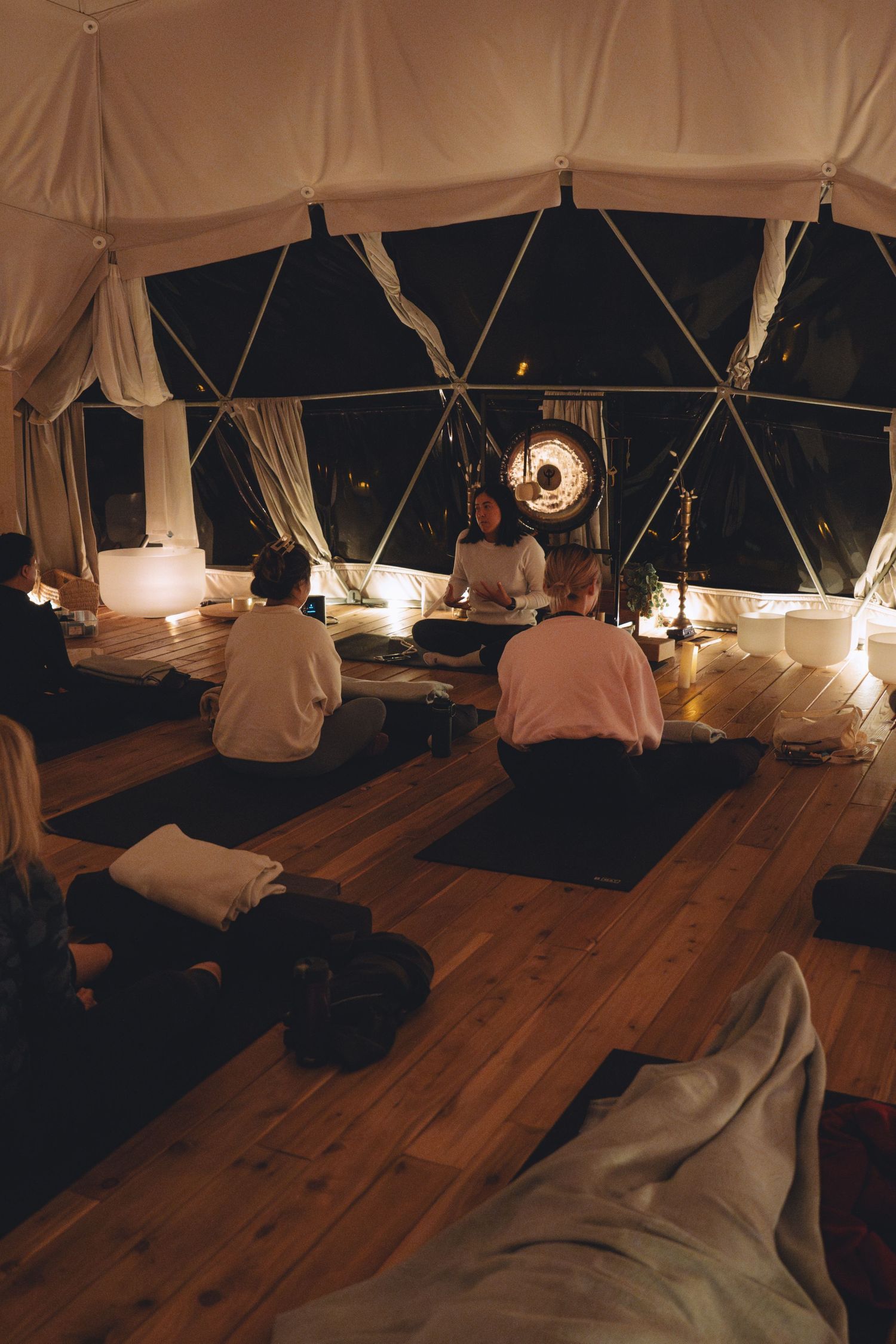 A candlelit yoga or meditation session takes place inside a geodesic dome tent with wooden flooring.