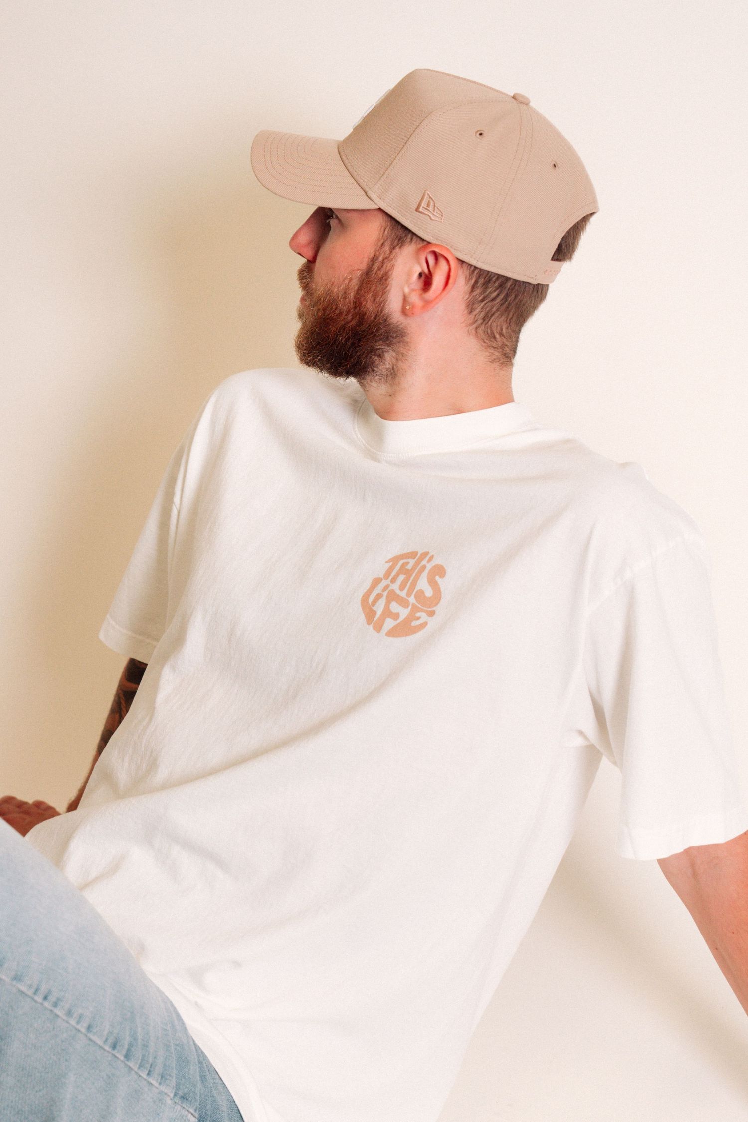 Person in baseball cap and white t-shirt with small logo shown from behind.