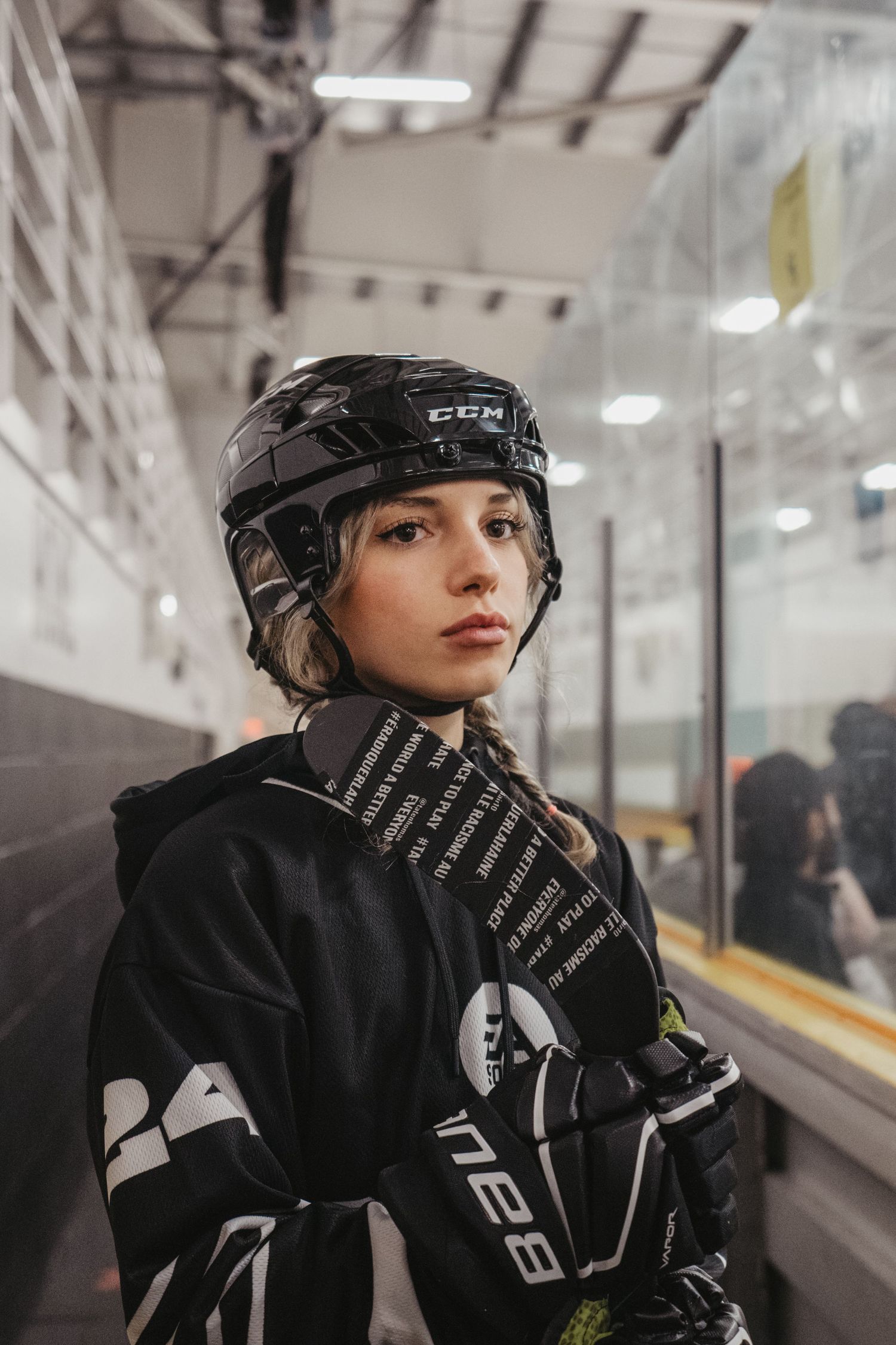 Hockey player wearing protective gear stands against wall in arena corridor.
