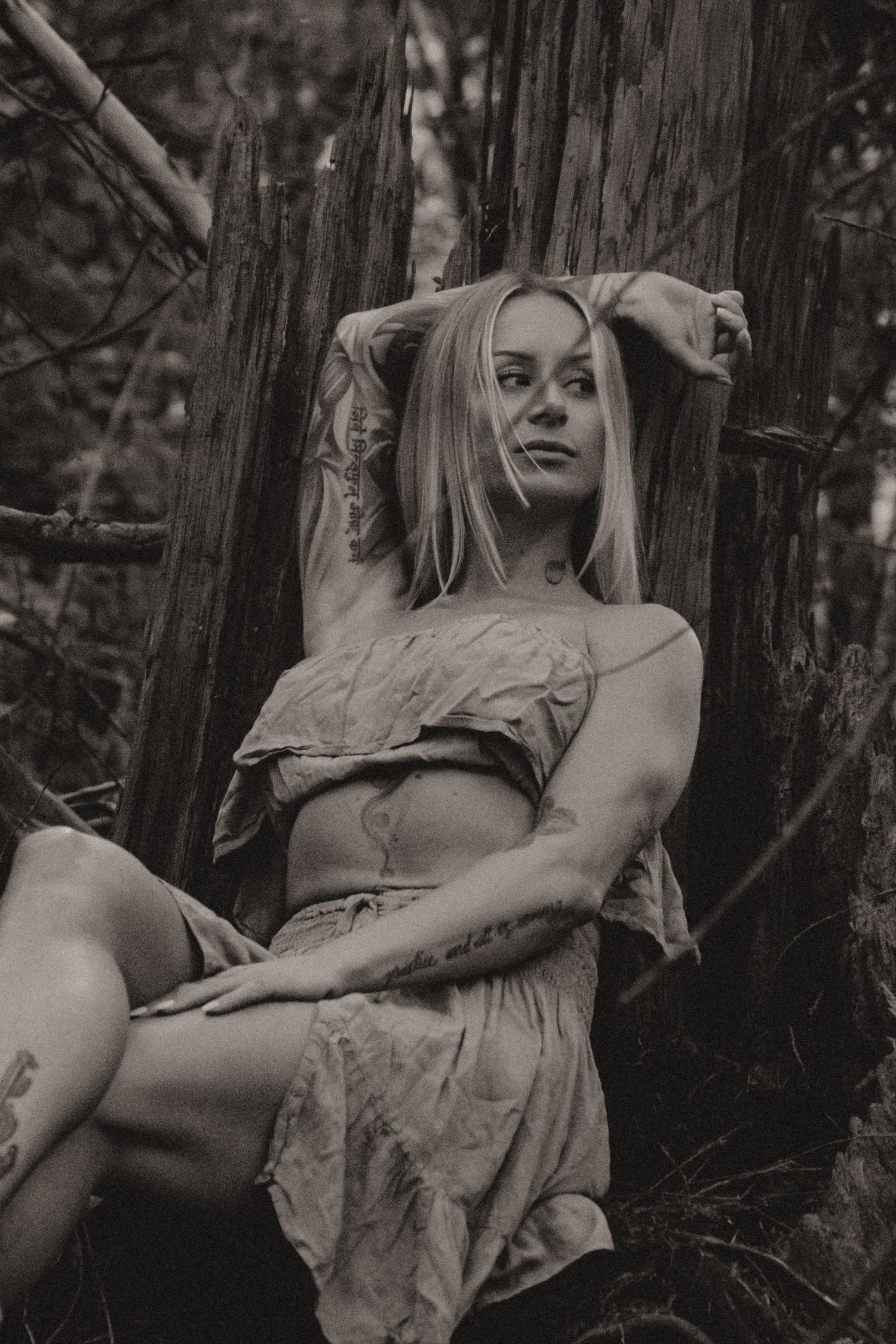 Artistic portrait in sepia tones showing a dreamy pose against a rustic tree trunk.
