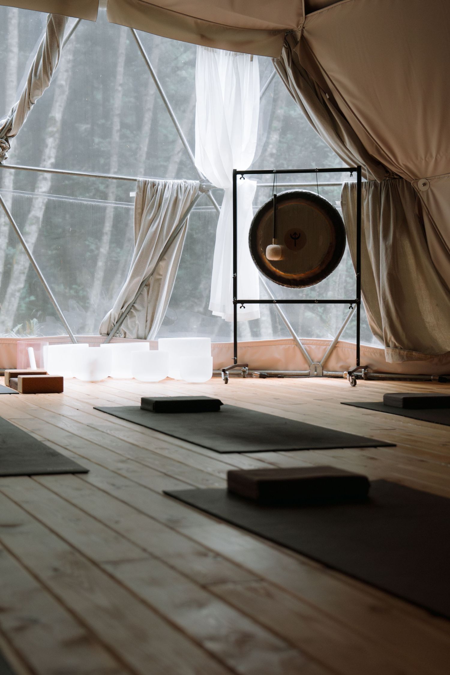 Meditation space with yoga mats and gong in tent-like structure with natural light.