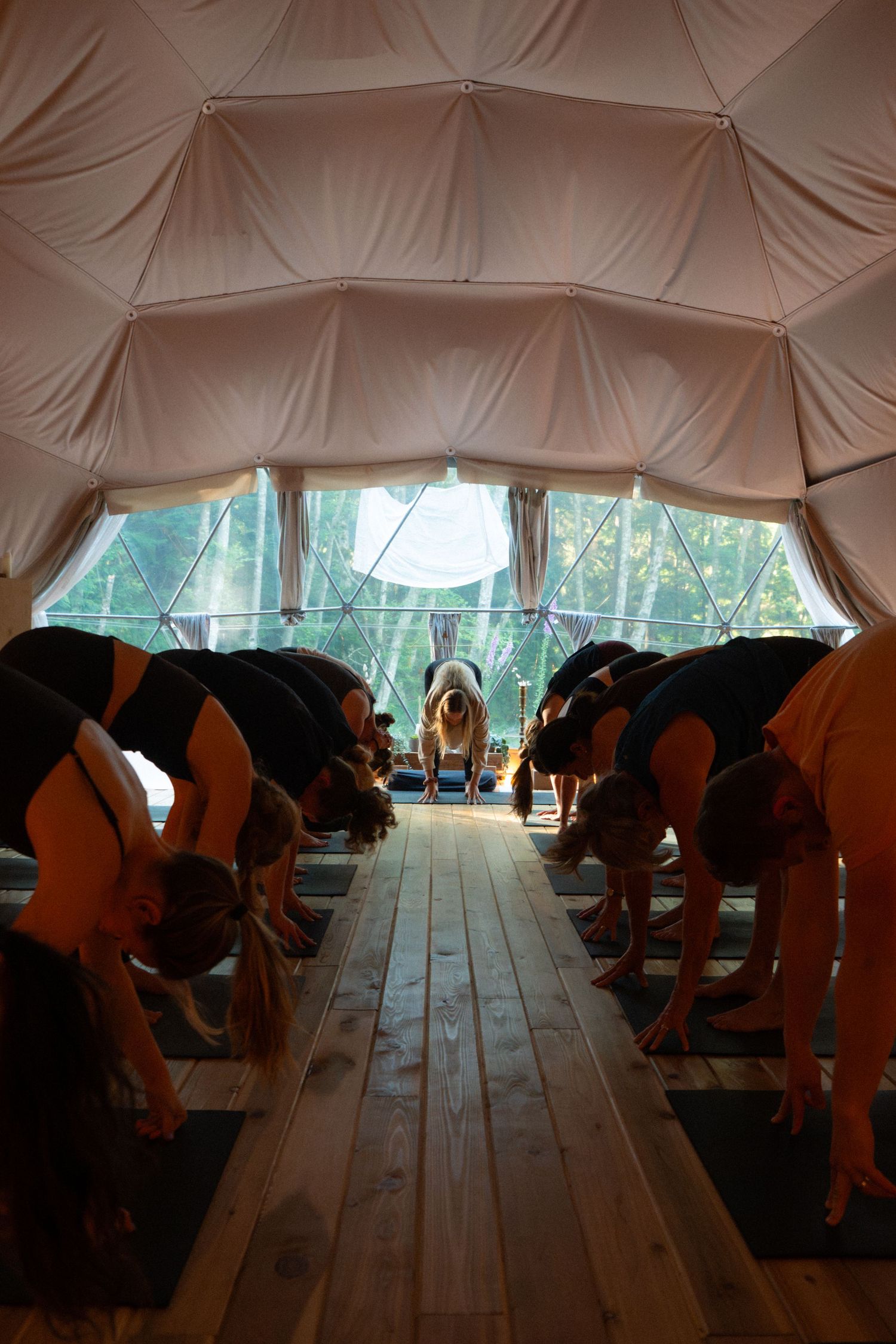 Students practice yoga poses in a sunlit geodesic dome studio with fabric ceiling panels.