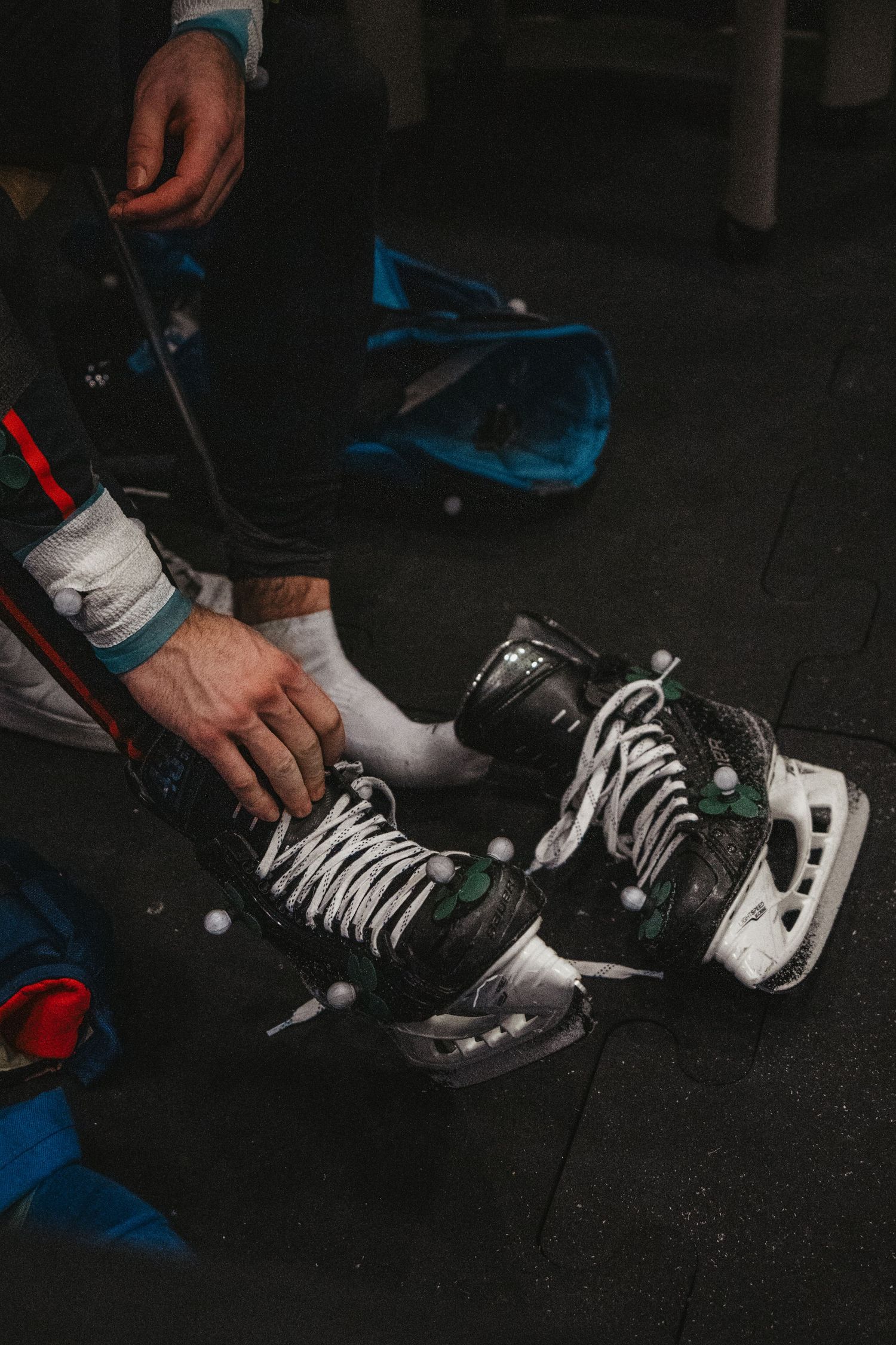 Hands tying laces on black hockey skates with white laces on dark floor.