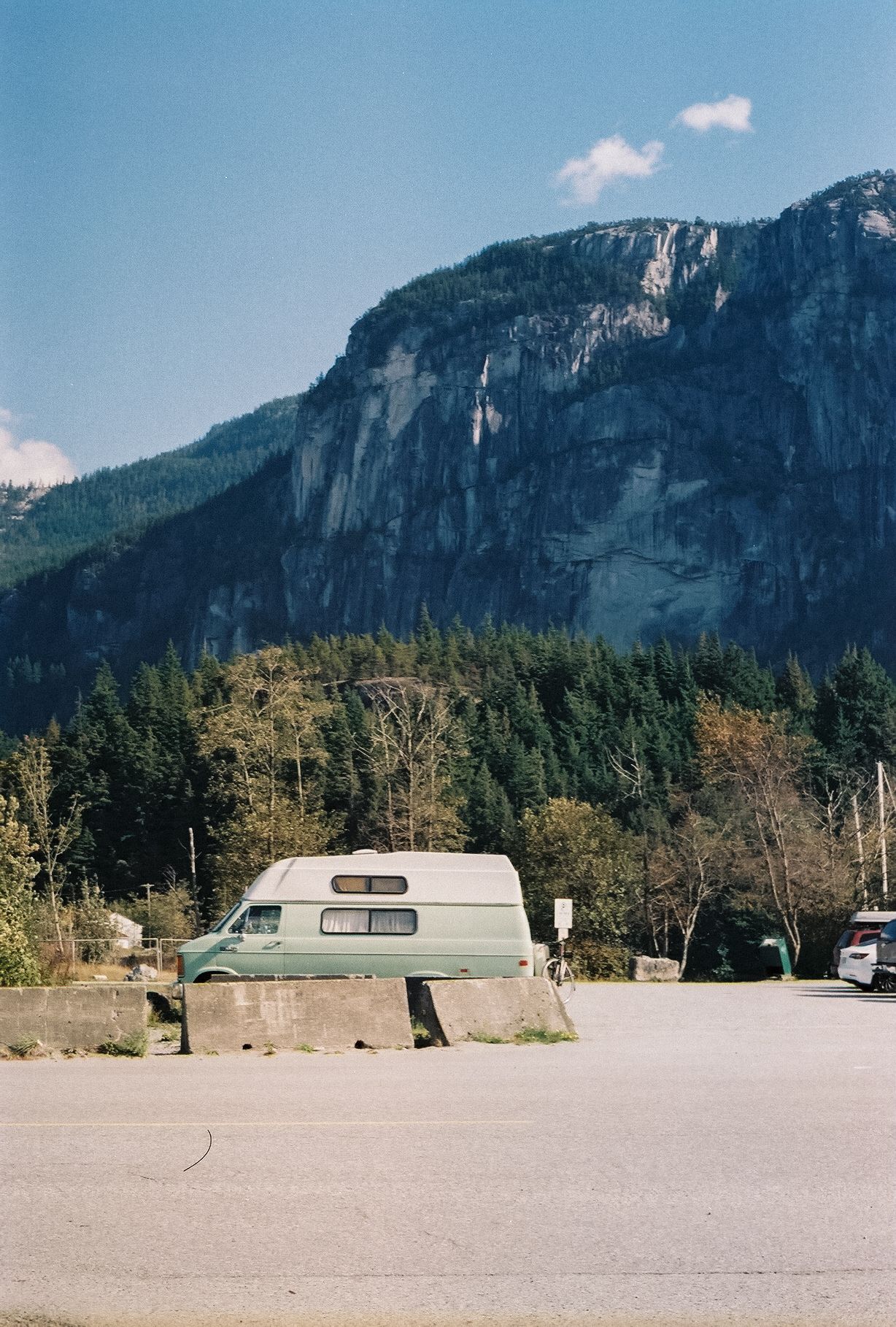 Parked camper van in lot with dramatic mountain cliff face rising in background.