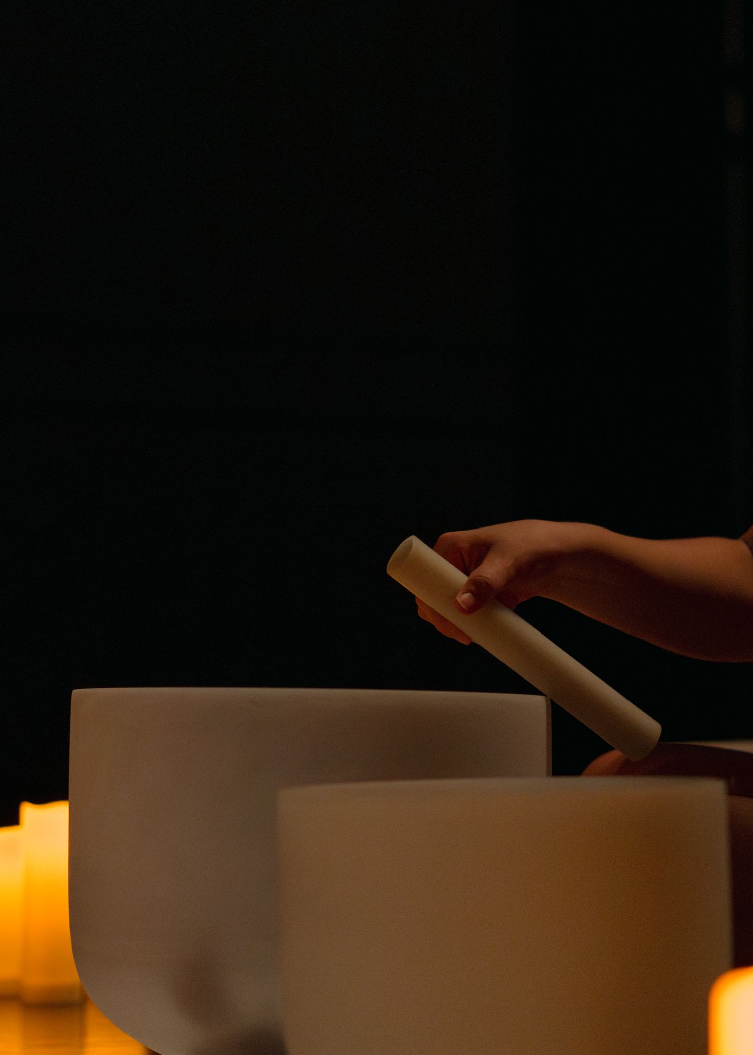 Hand reaching for crystal singing bowls with glowing candles in dark atmospheric setting.