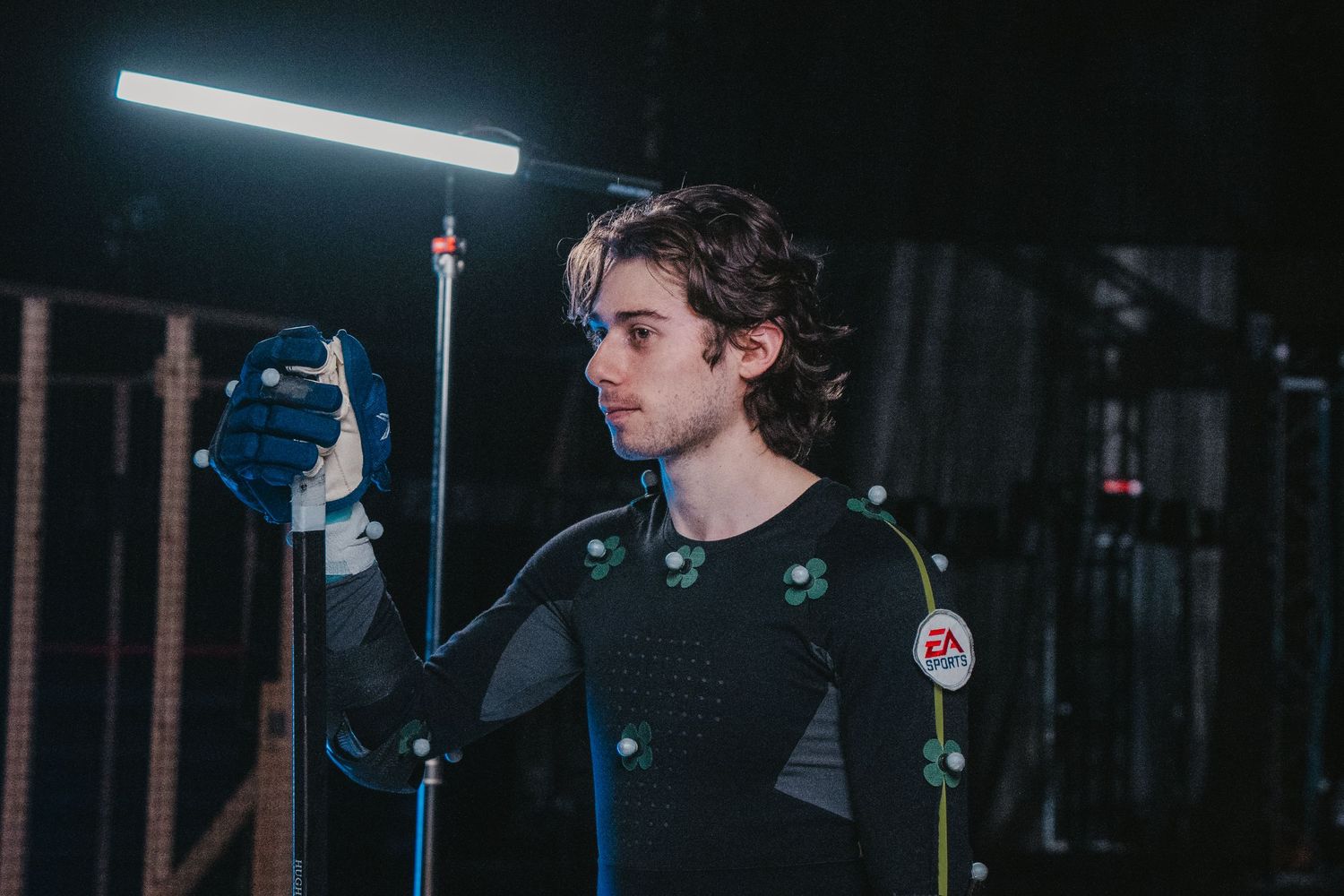 Motion capture performer in dark studio with overhead lighting and tracking markers on suit.