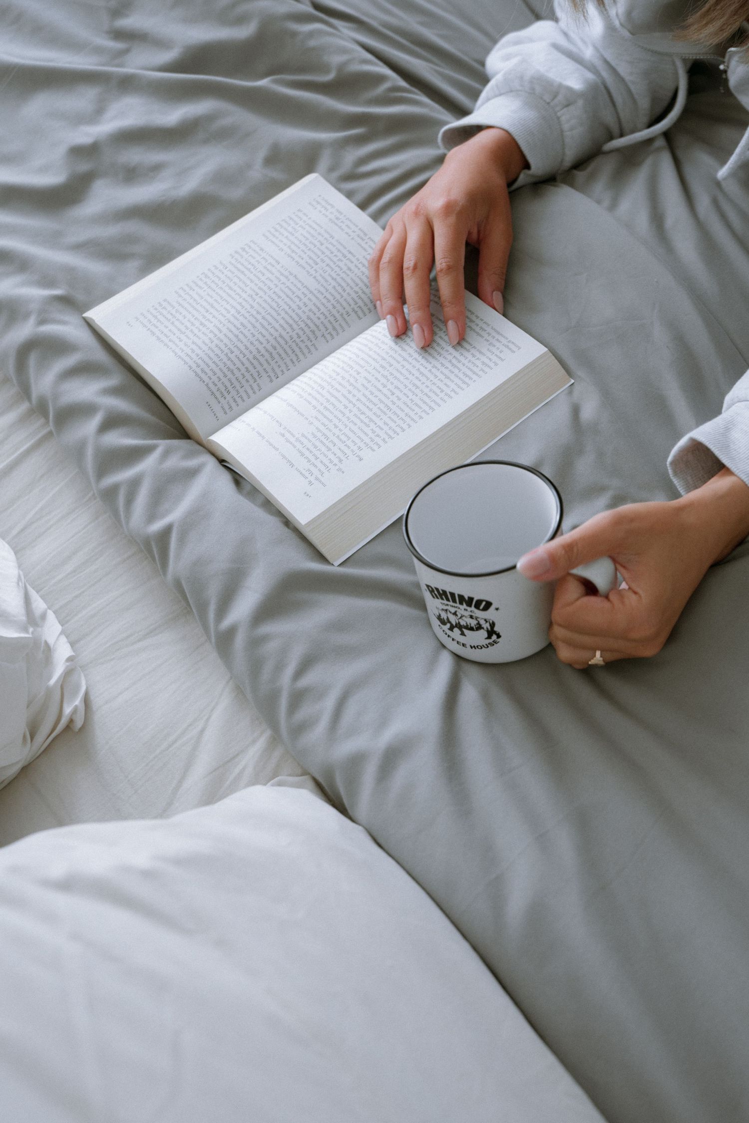 White bedding with an open book and coffee mug showing cozy reading time.