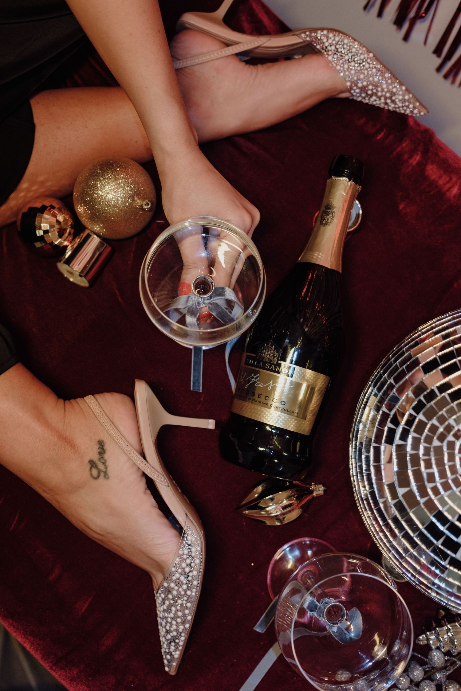 Elegant party setup with champagne, martini glasses, and sparkly heels on velvet surface.