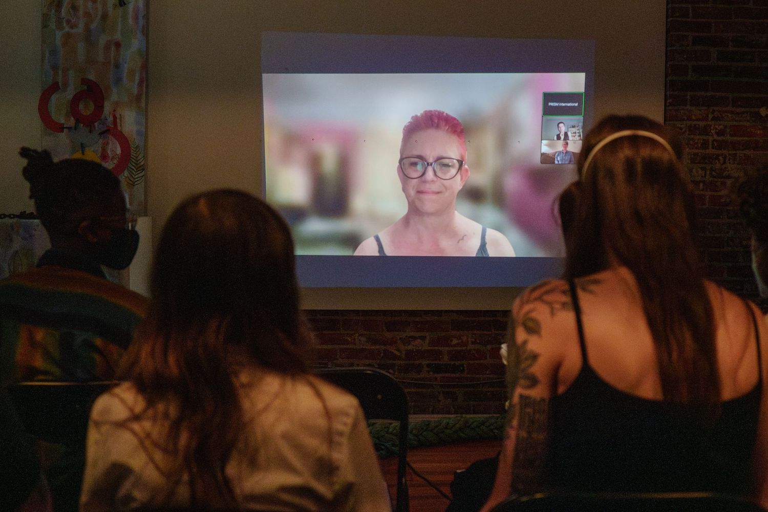 Audience members watch a projected video presentation in a dimly lit room.
