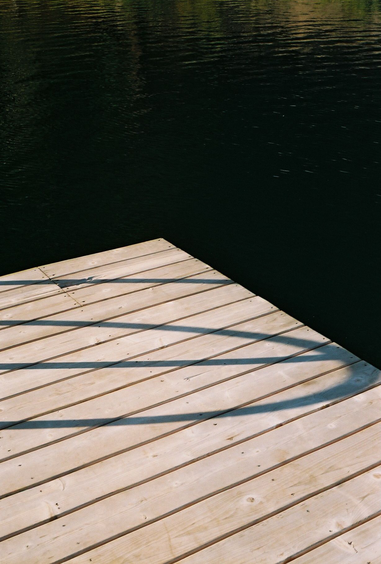 Wooden dock planks cast diagonal shadows over calm dark water.