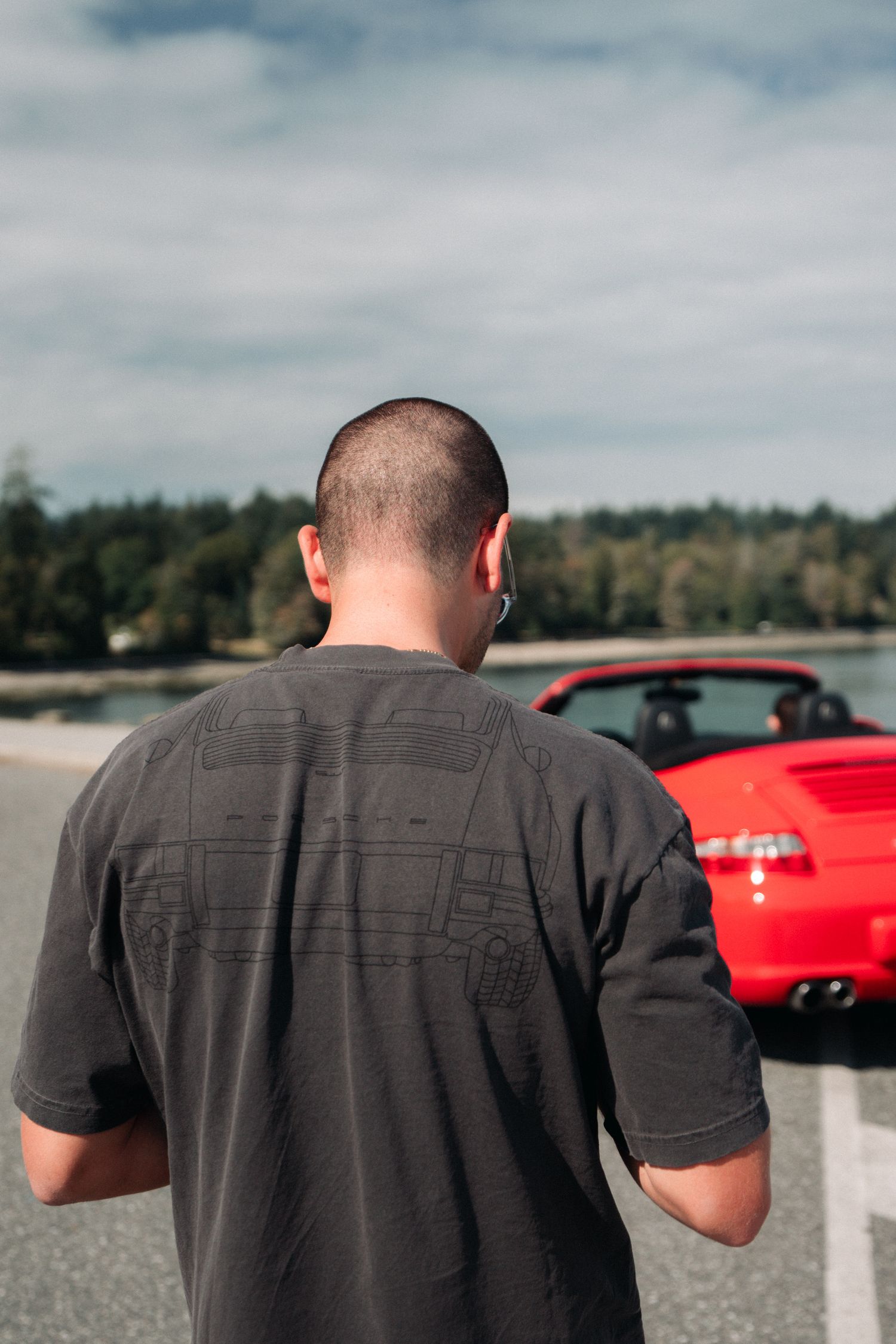 Person in a dark t-shirt standing near a parked red sports car.