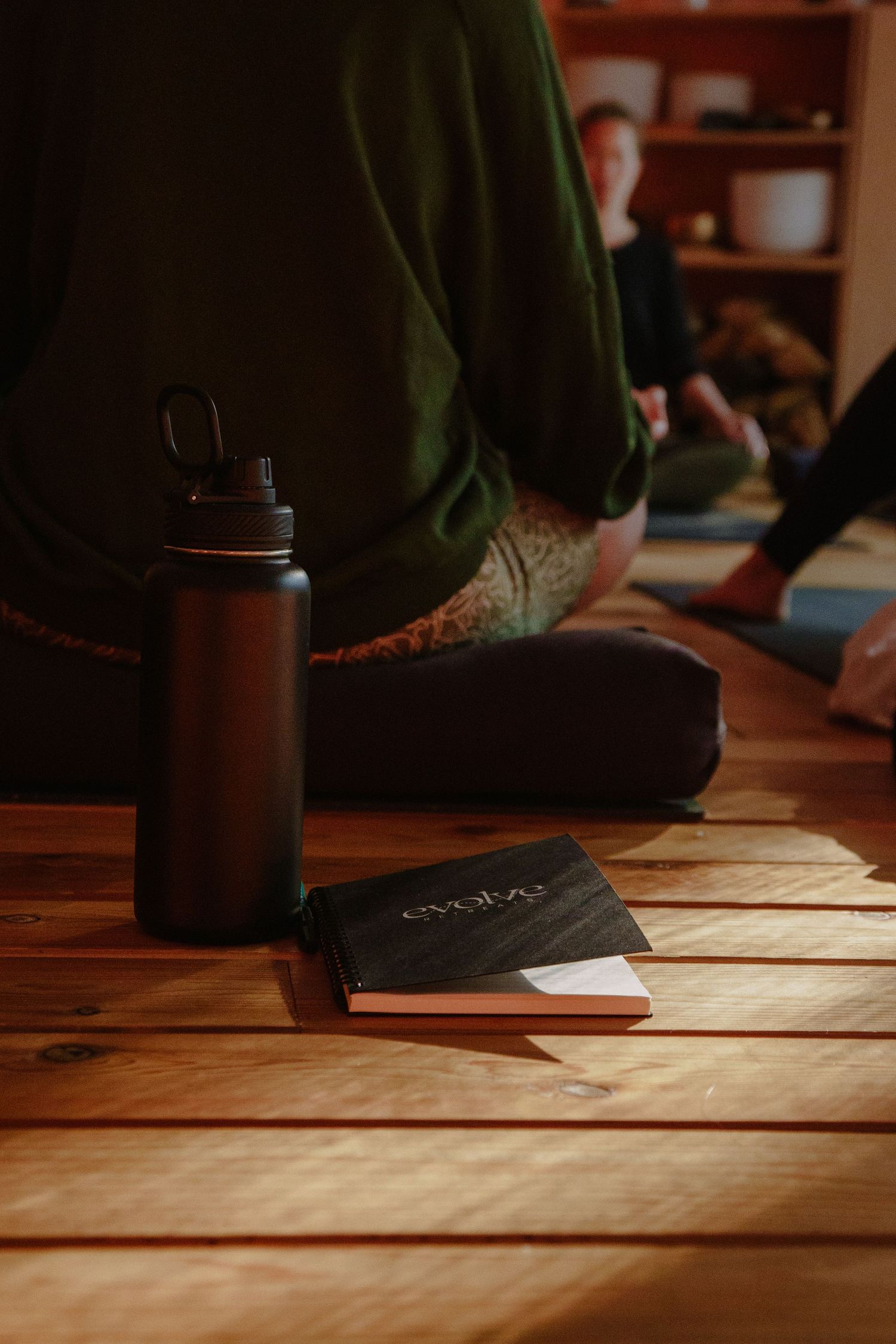 A water bottle and notebook rest on wooden floorboards during a yoga session.