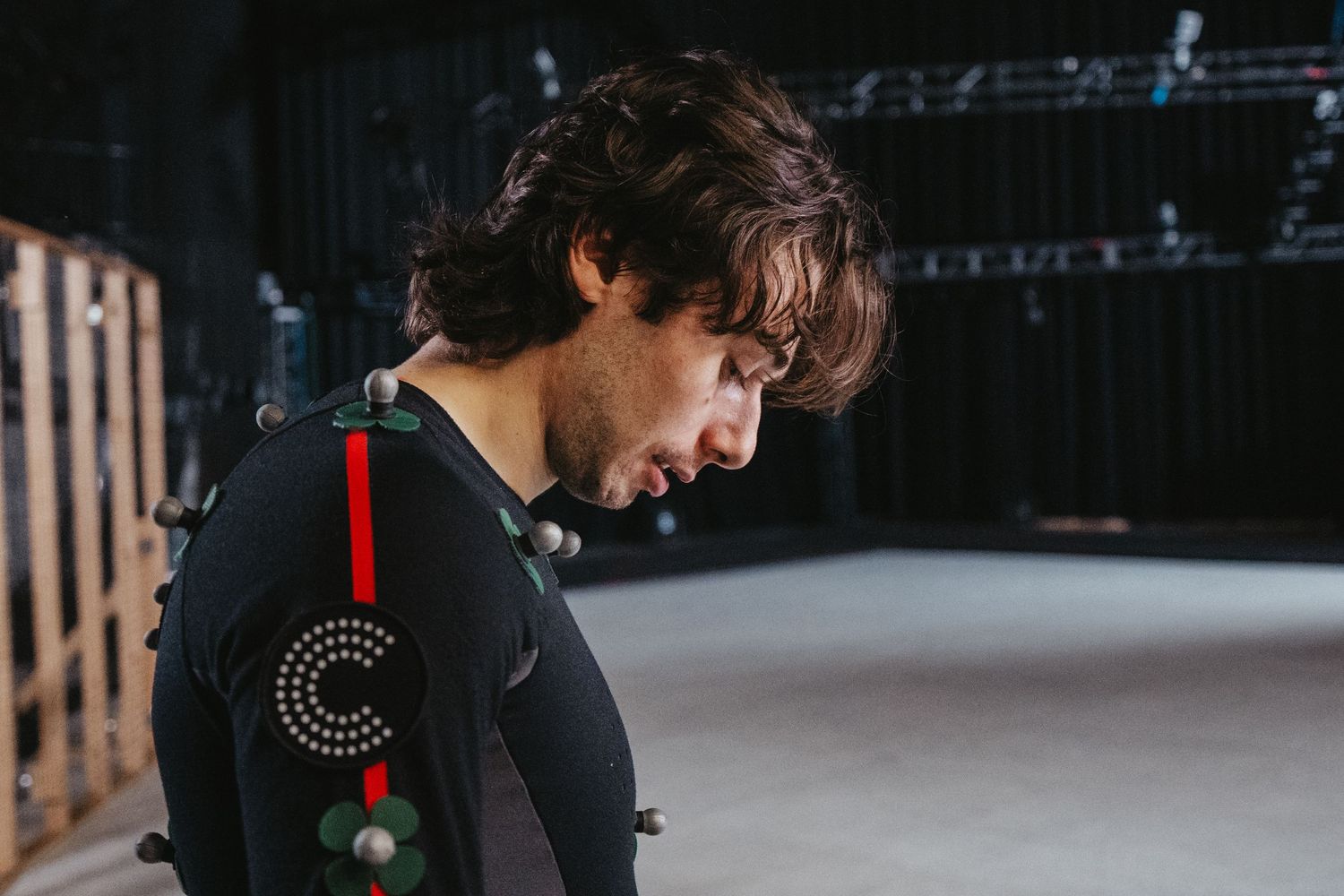 Side view of performer wearing motion capture suit with tracking markers in studio setting.