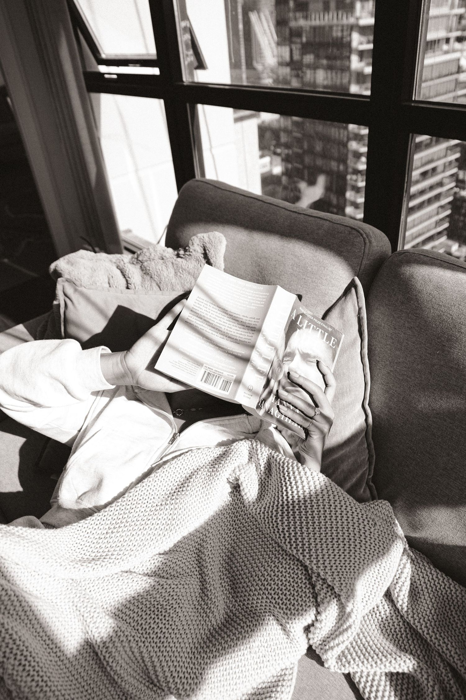 Black and white photo of book and blankets by city window.